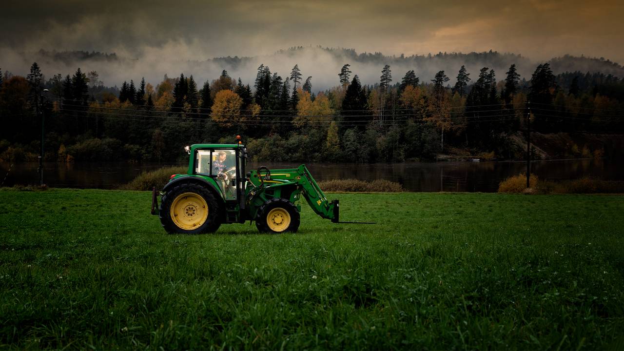 En traktor kjører over et jorde i kveldslys og med tunge skyer
