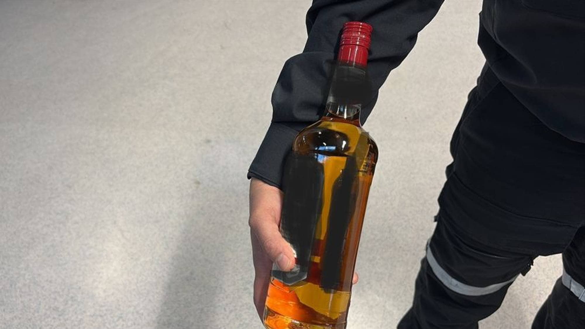 En flaske uten etikett med lysebrunt innhold holdes av en mann i tolluniform