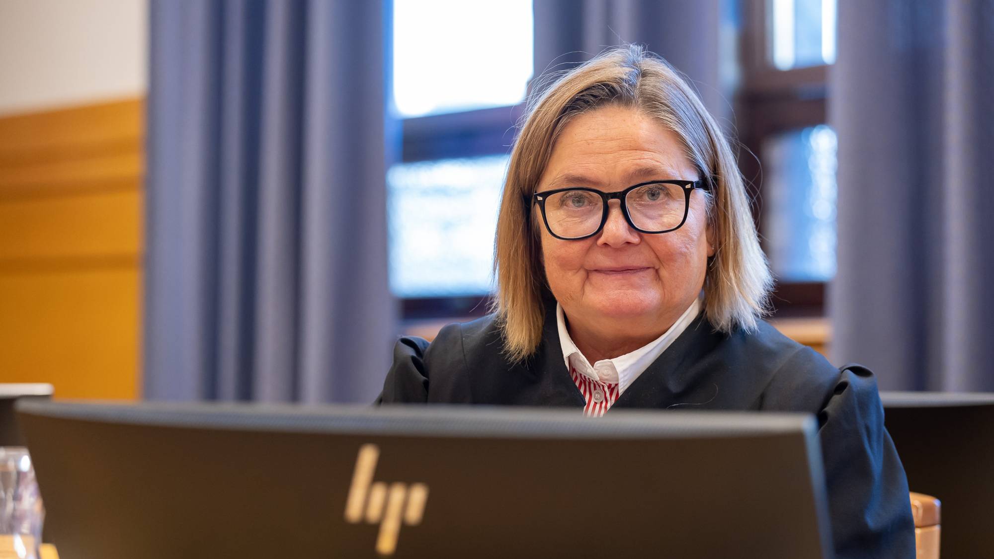 Statsadvokat Kaia Strandjord er i en rettssal i Trøndelag tingrett. Hun er iført svart kappe og kikker mot fotografen. Strandjord smiler forsiktig