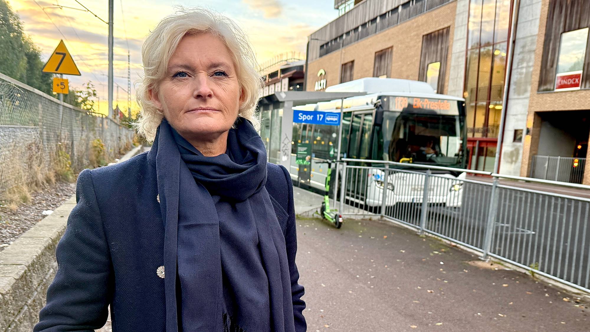 En kvinne som står på en vei med en buss bak seg