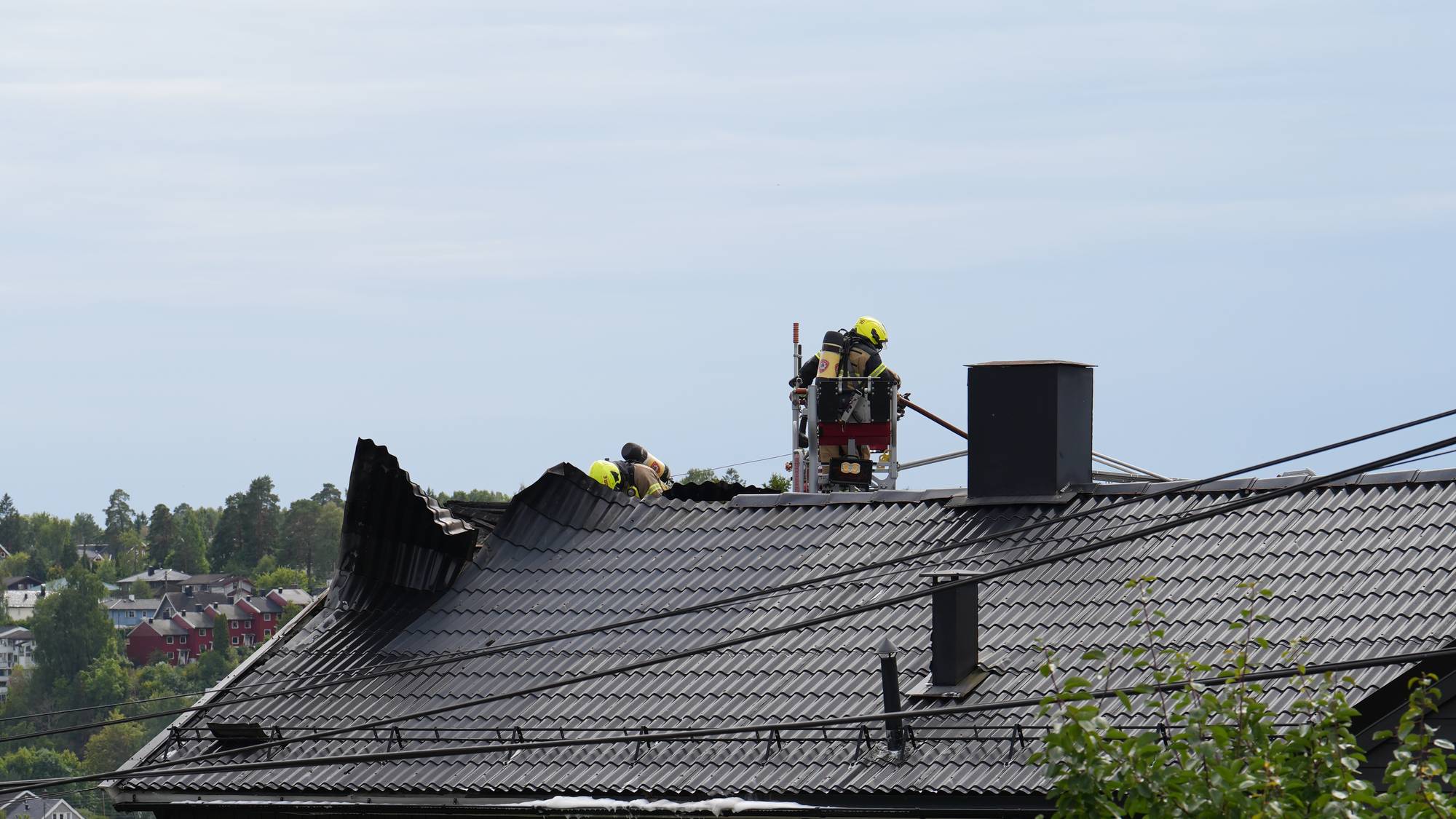 Brannmannskaper arbeider på taket av en mørk bolig med brannstige. (Bildebeskrivelsen er laget av en KI-tjeneste)