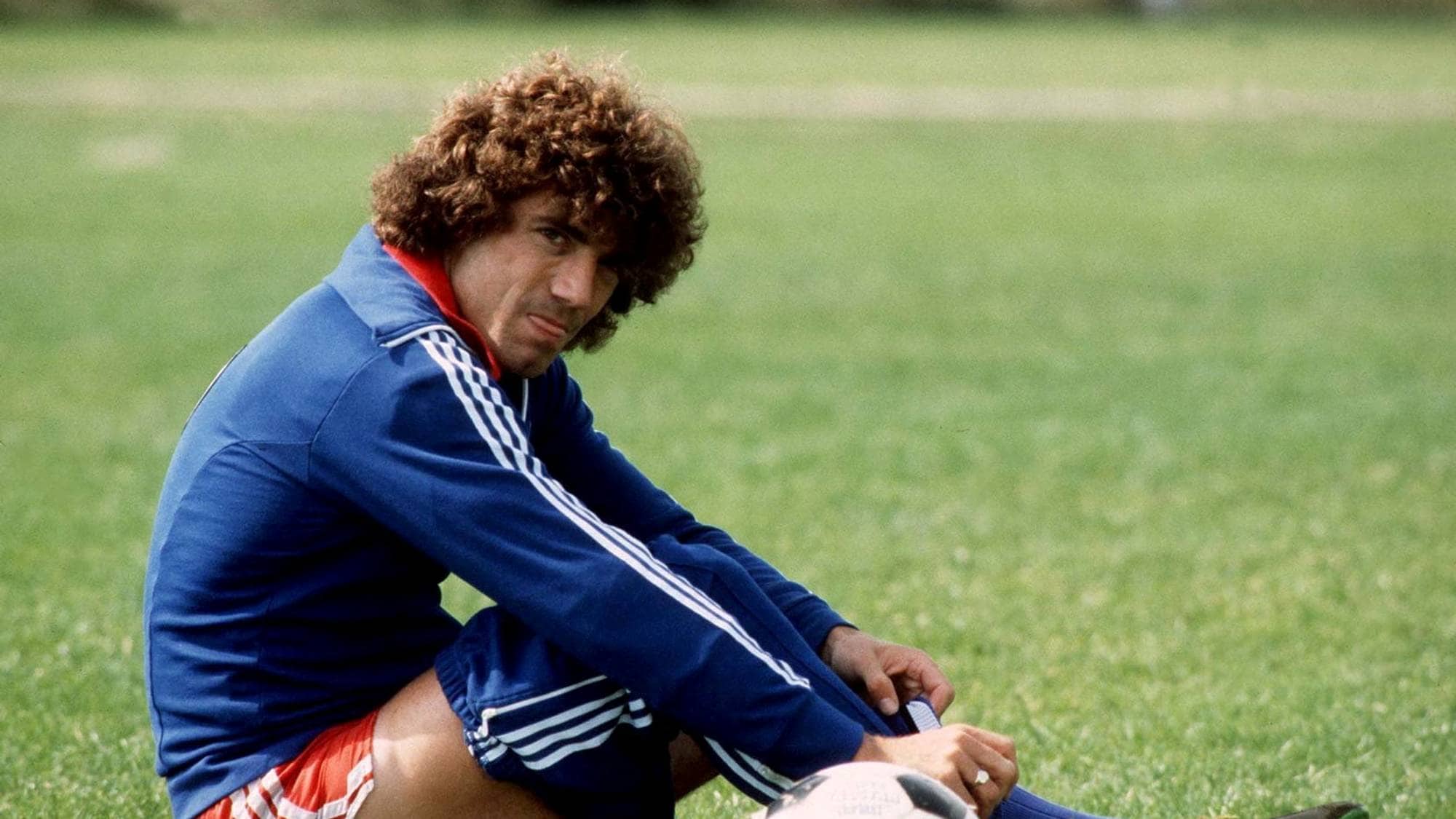 Fotballspiller Kevin Keegan sitter på en gressbane og tar på seg fotballskoene. (Bildebeskrivelsen er laget av en KI-tjeneste)