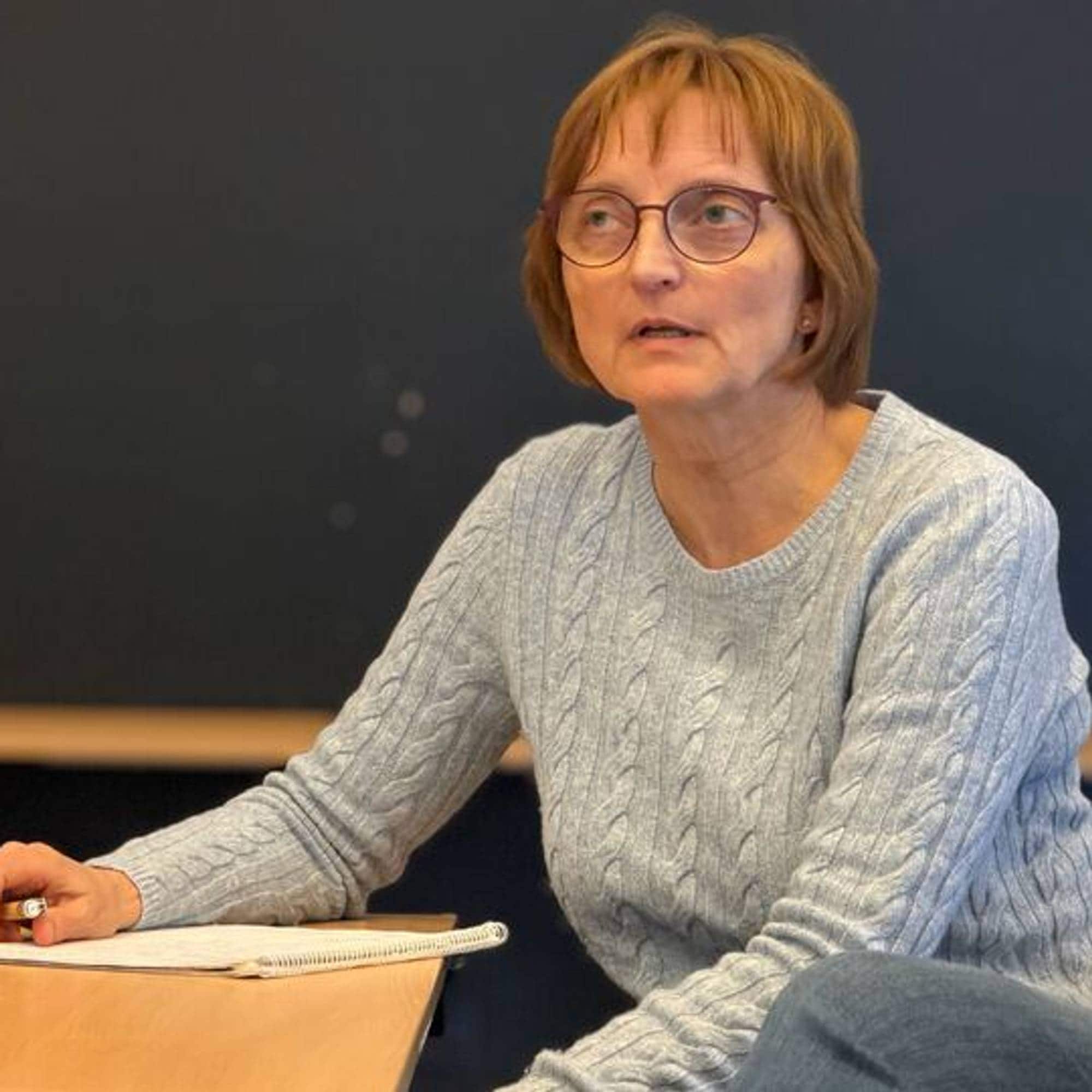 En dame som sitter ved et bord med kort hår og briller. 