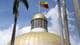 Fausto Torrealba / Reuters / NTB Bildet viser kuppelen på en bygning med en gullfarget topp, hvor Venezuelas flagg vaier i vinden. Omgivelsene inkluderer palmer som strekker seg oppover mot en delvis skyet himmel. Det er ingen personer til stede i bildet. Bygningens stil og flagget kan indikere en offentlig eller politisk kontekst. (Bildebeskrivelsen er laget av en KI-tjeneste)