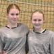 Privat To personer står tett sammen iført grå sportsdrakter med logo på brystet. De poserer foran et håndballmål med nett. Begge har kort hår og smiler. Omgivelsene indikerer at bildet er tatt i en sportshall. (Bildebeskrivelsen er laget av en KI-tjeneste)