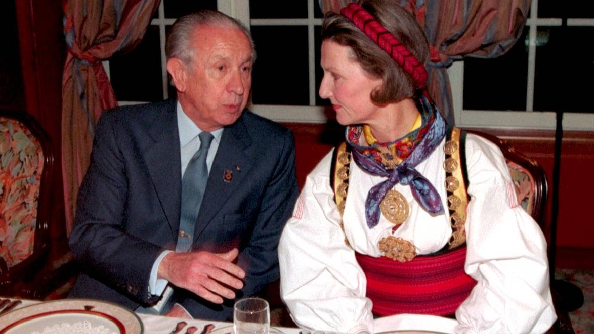 Prinsesse Astrid sitter ved et bord og snakker med en mann i dress. (Bildebeskrivelsen er laget av en KI-tjeneste)
