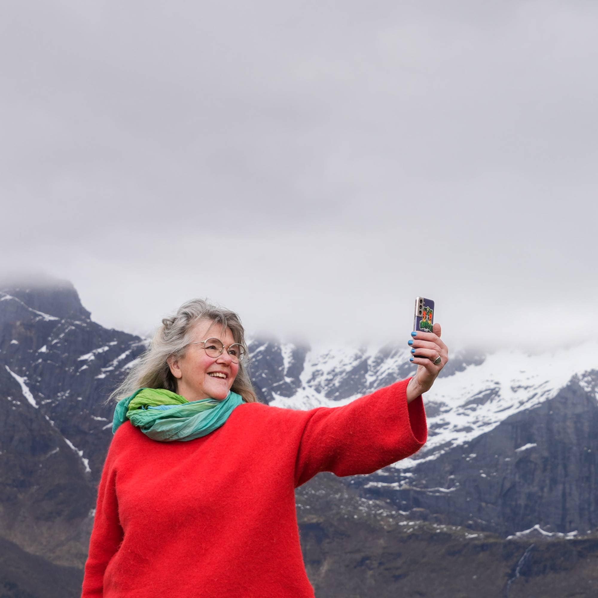 En kvinne i rød genser, grått hår og briller smiler til kamera.