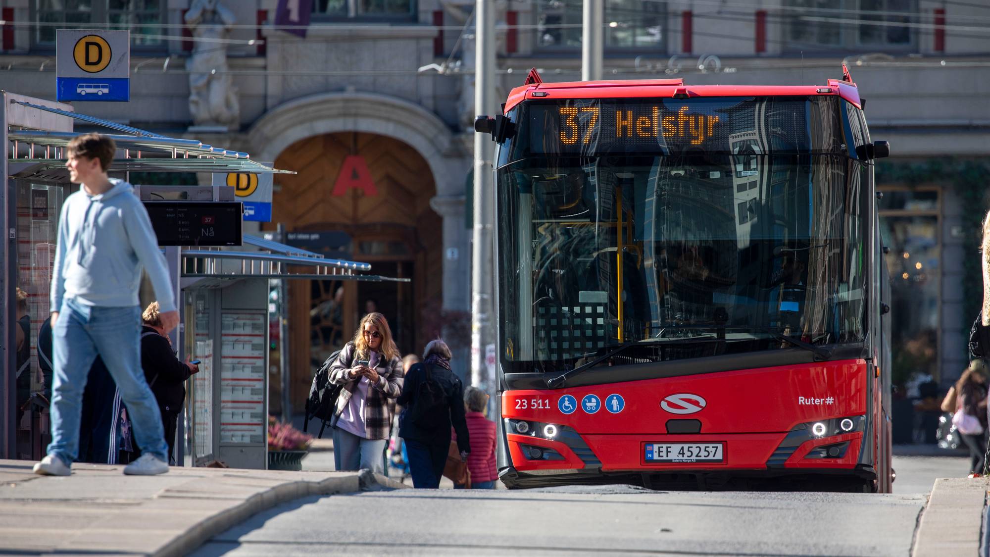 Ruter-buss linje 37 til Helsfyr kjører inn til et busstopp i Oslo med ventende passasjerer. (Bildebeskrivelsen er laget av en KI-tjeneste)