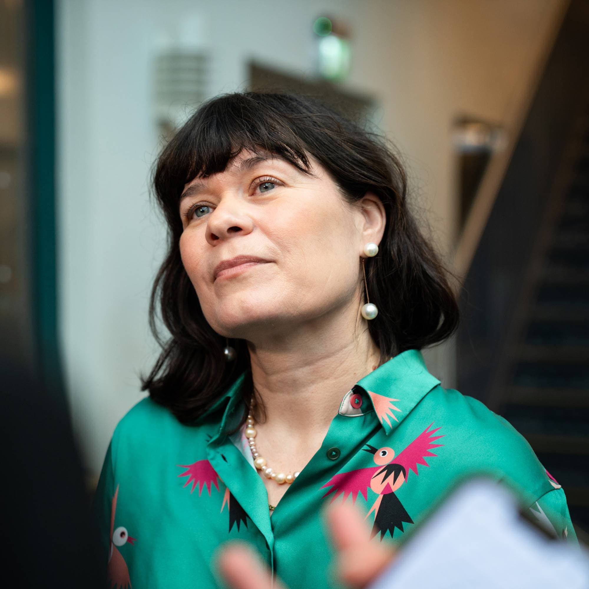 kvinne med brunt kort hår med lugg, i grønn skjorte med rosa fugler 