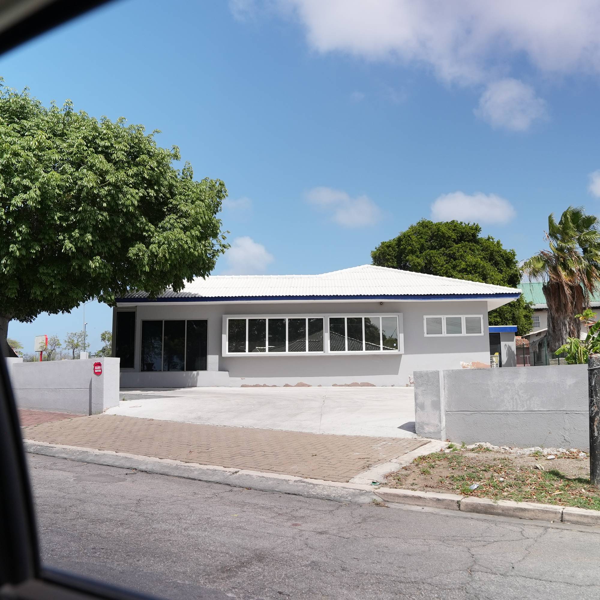 Foto ut av et bilvindu mot et grått hus i varmere strøk