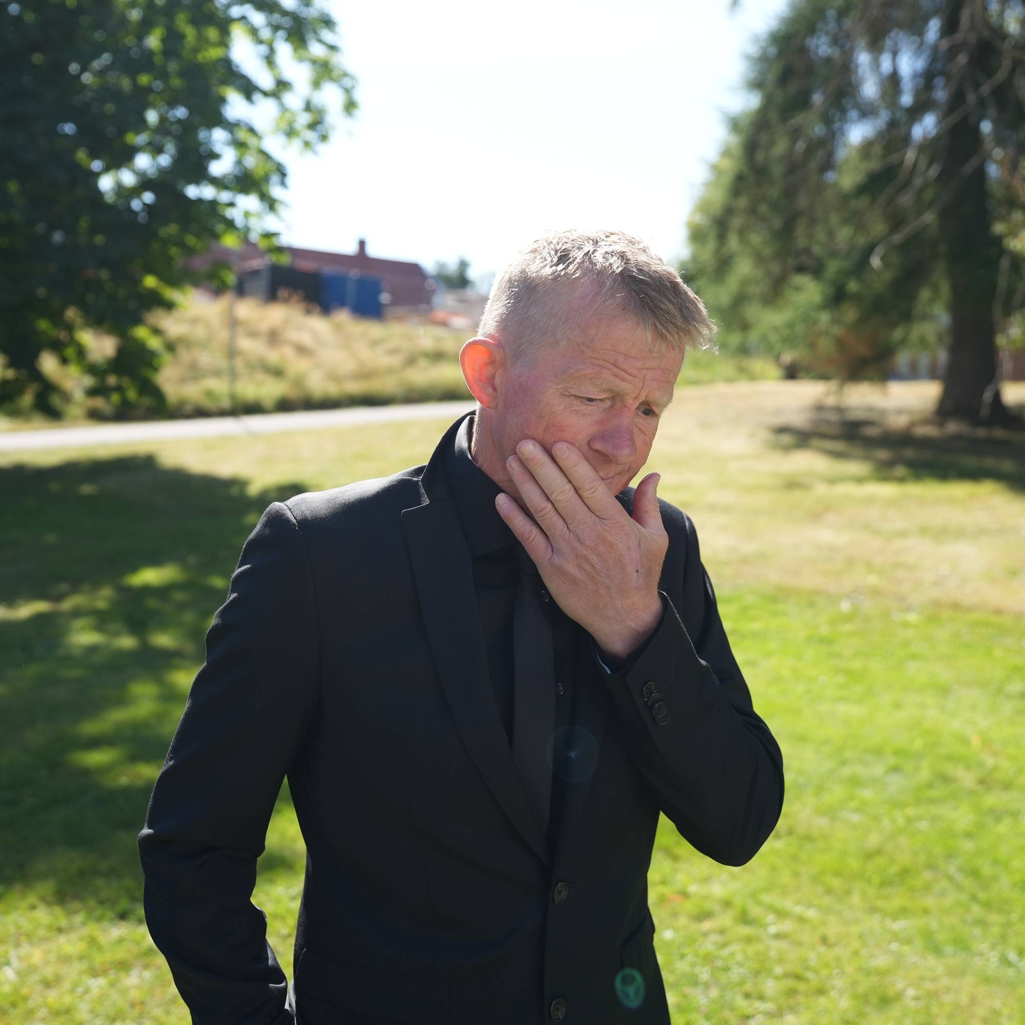 En mann i svart dress står utendørs med hånden mot ansiktet og ser ned. (Bildebeskrivelsen er laget av en KI-tjeneste)