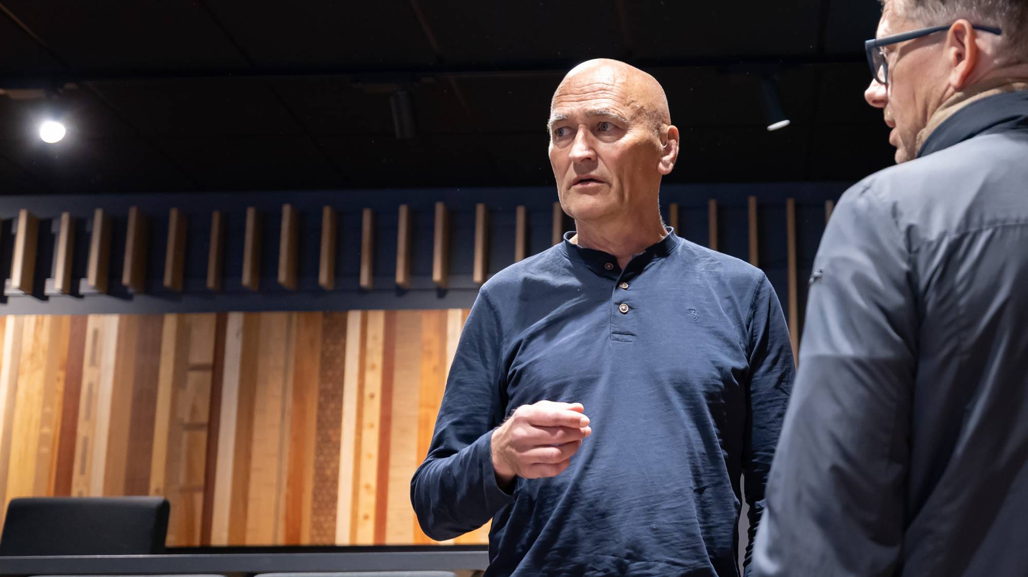 Harry Arne Solberg står i et auditorium. Han snakker med en person som vi kun ser deler av ansiktet til.