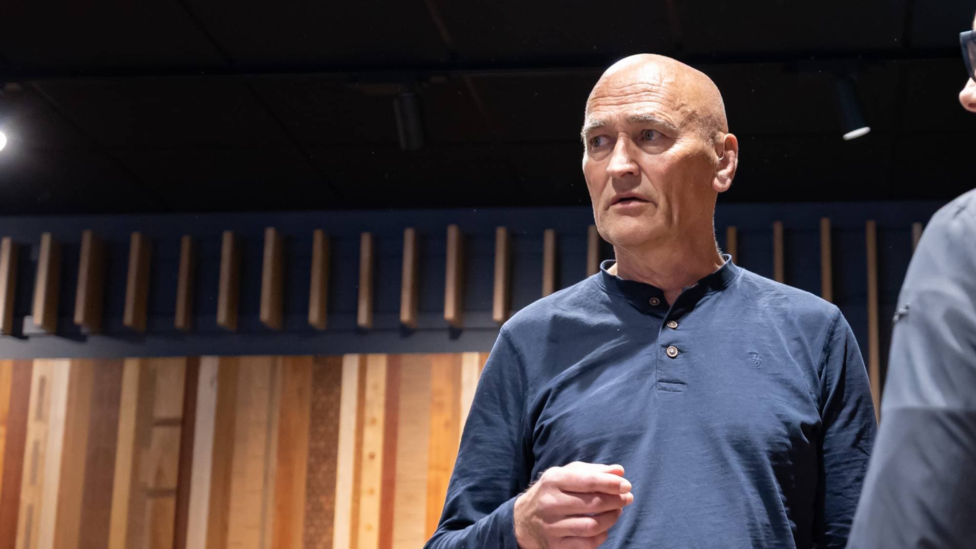 Harry Arne Solberg står i et auditorium. Han snakker med en person som vi kun ser deler av ansiktet til.