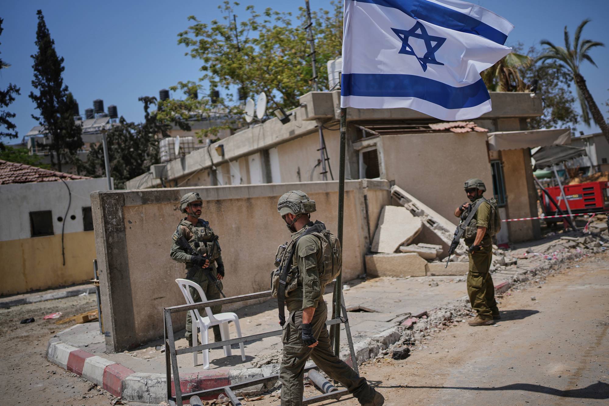 en gruppe soldater som står utenfor en delvis ødelagt bygning, et israelsk flagg veiver i vinden