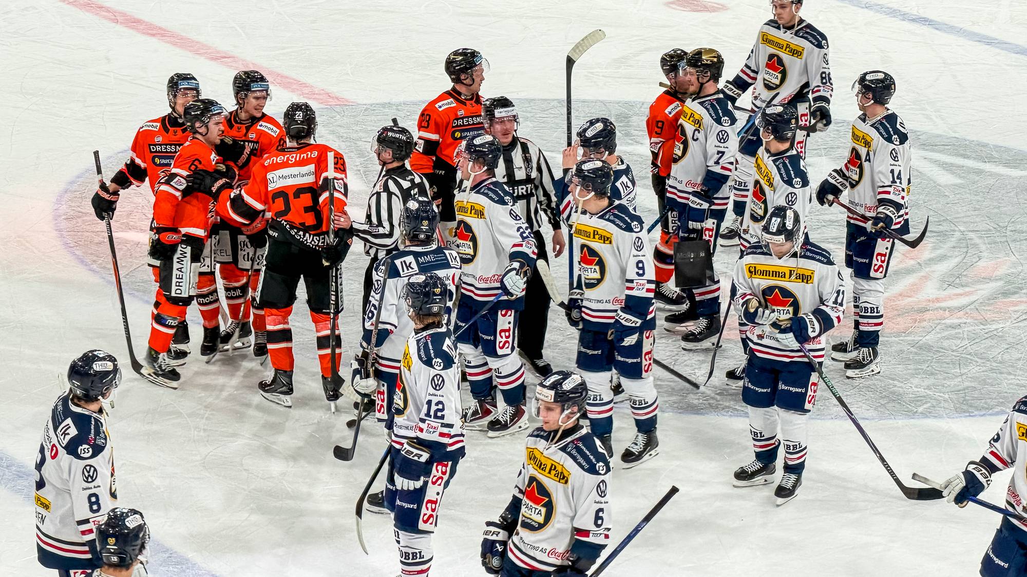 Ishockeyspillere fra to lag og dommere samlet på isen etter en kamp. (Bildebeskrivelsen er laget av en KI-tjeneste)