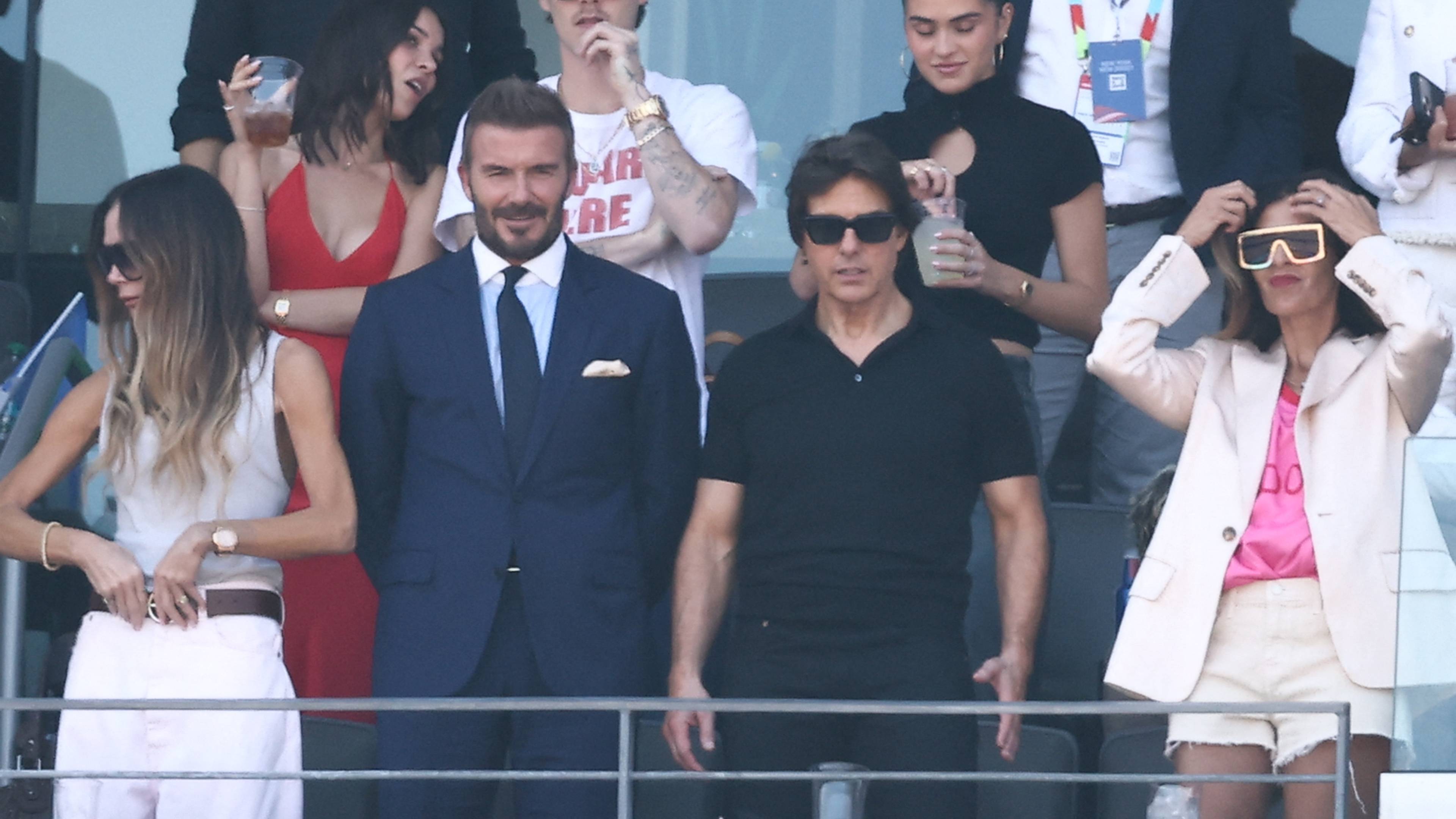 David Beckham og Tom Cruise sitter sammen med andre på en tribune under et sportsarrangement. (Bildebeskrivelsen er laget av en KI-tjeneste)