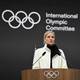 DANIEL MUNOZ / AFP / NTB En person står foran en mikrofonsstativ på en scene med den internasjonale olympiske komitéens logo synlig i bakgrunnen. Personen er kledd i en hvit jakke og har en svart skjerf rundt halsen. Det er en treplate foran dem med de olympiske ringene. Omgivelsene er mørke og fokusert på taleren, noe som gir en formell atmosfære. (Bildebeskrivelsen er laget av en KI-tjeneste)
