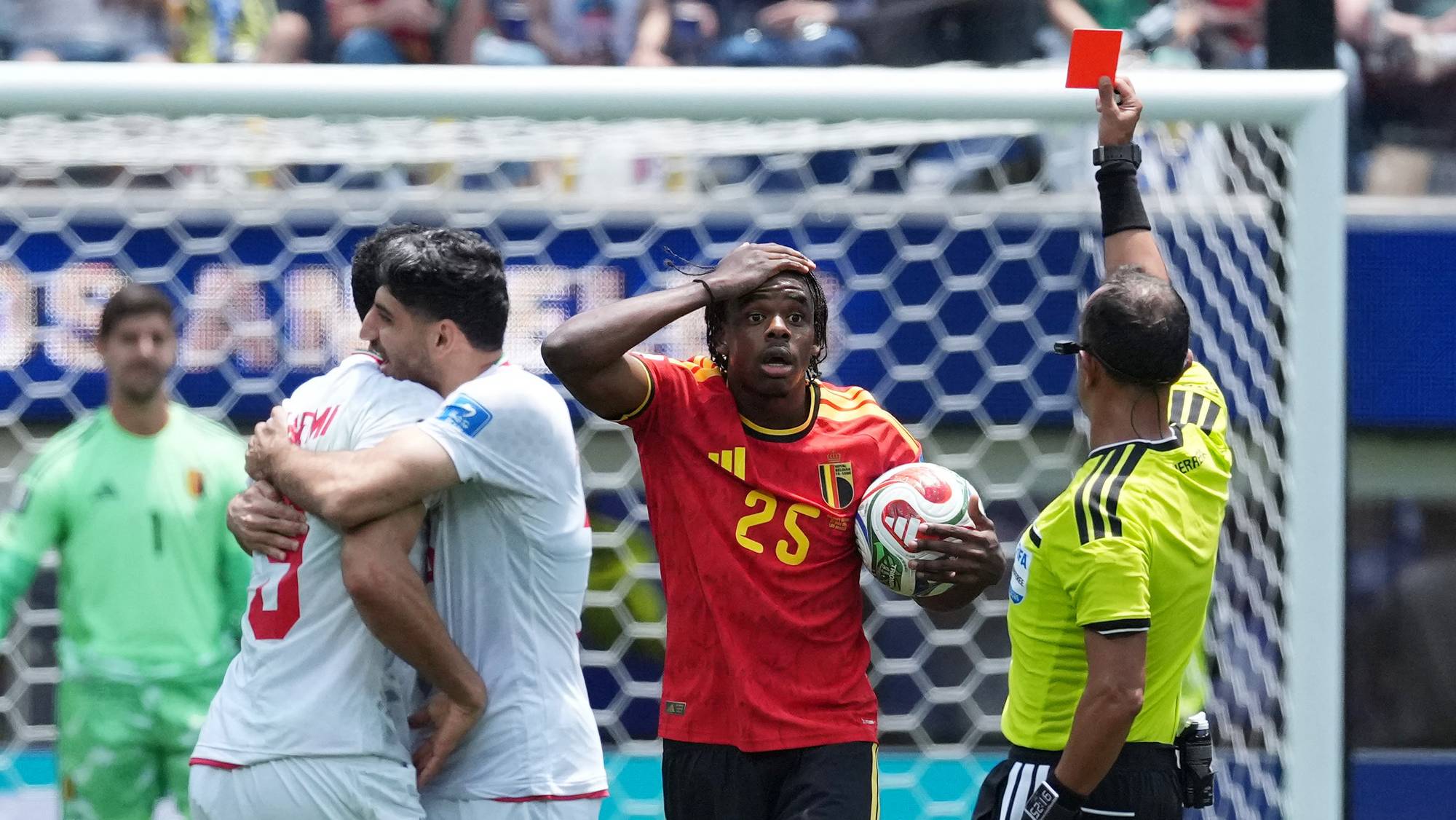 Dommeren viser et rødt kort til en belgisk spiller som holder en fotball. To iranske spillere gir hverandre en klem i bakgrunnen. En keeper i grønn drakt står lengre bak. (Bildebeskrivelsen er laget av en KI-tjeneste)