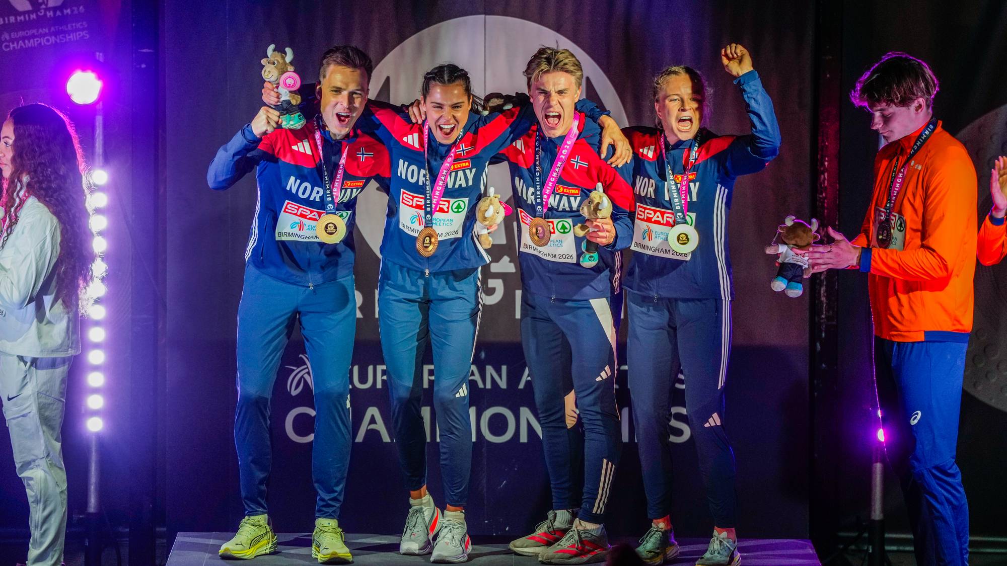 Fire personer på et podium med gullmedalje som jubler