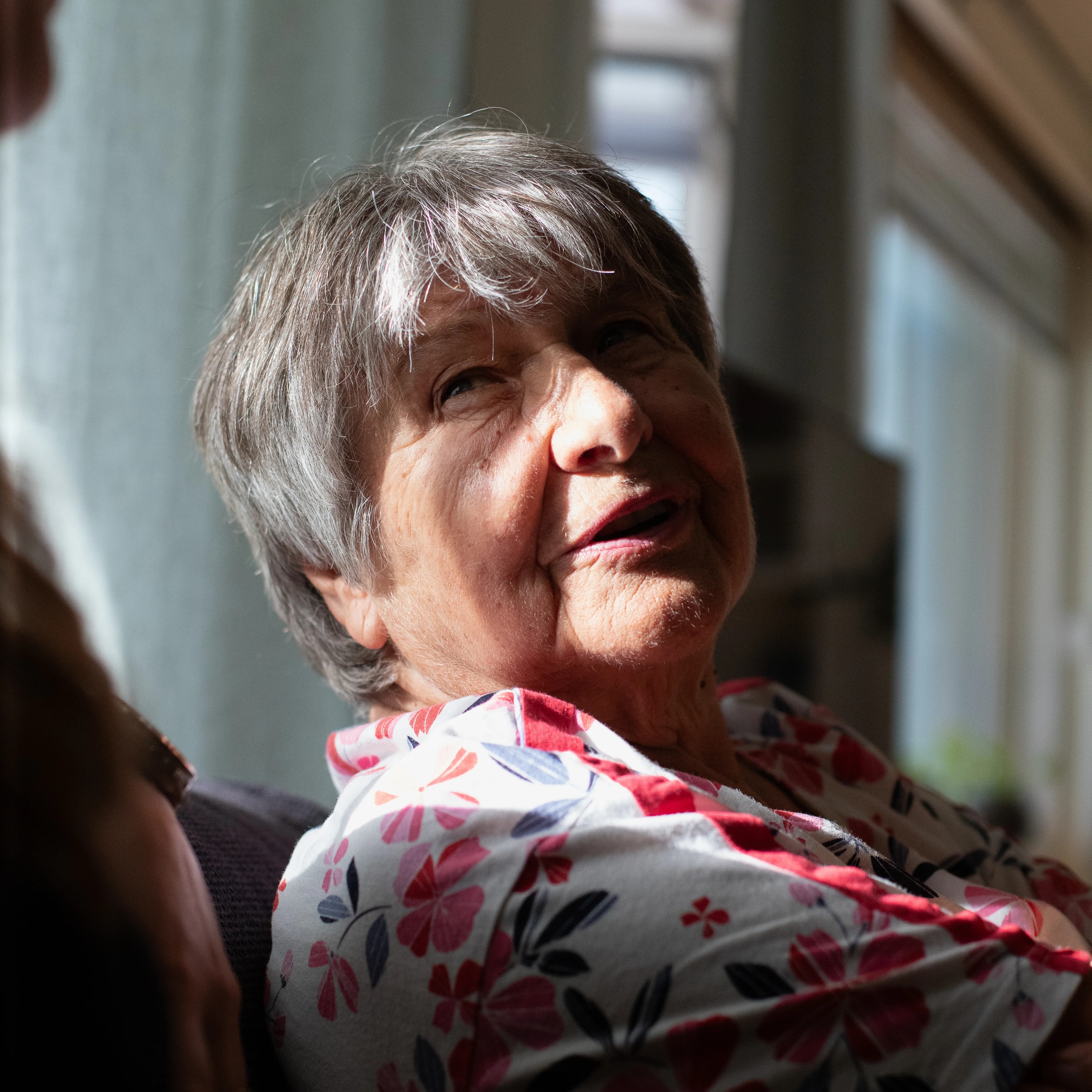 en eldre kvinne som sitter i en sofa, lys treffer ansiktet hennes