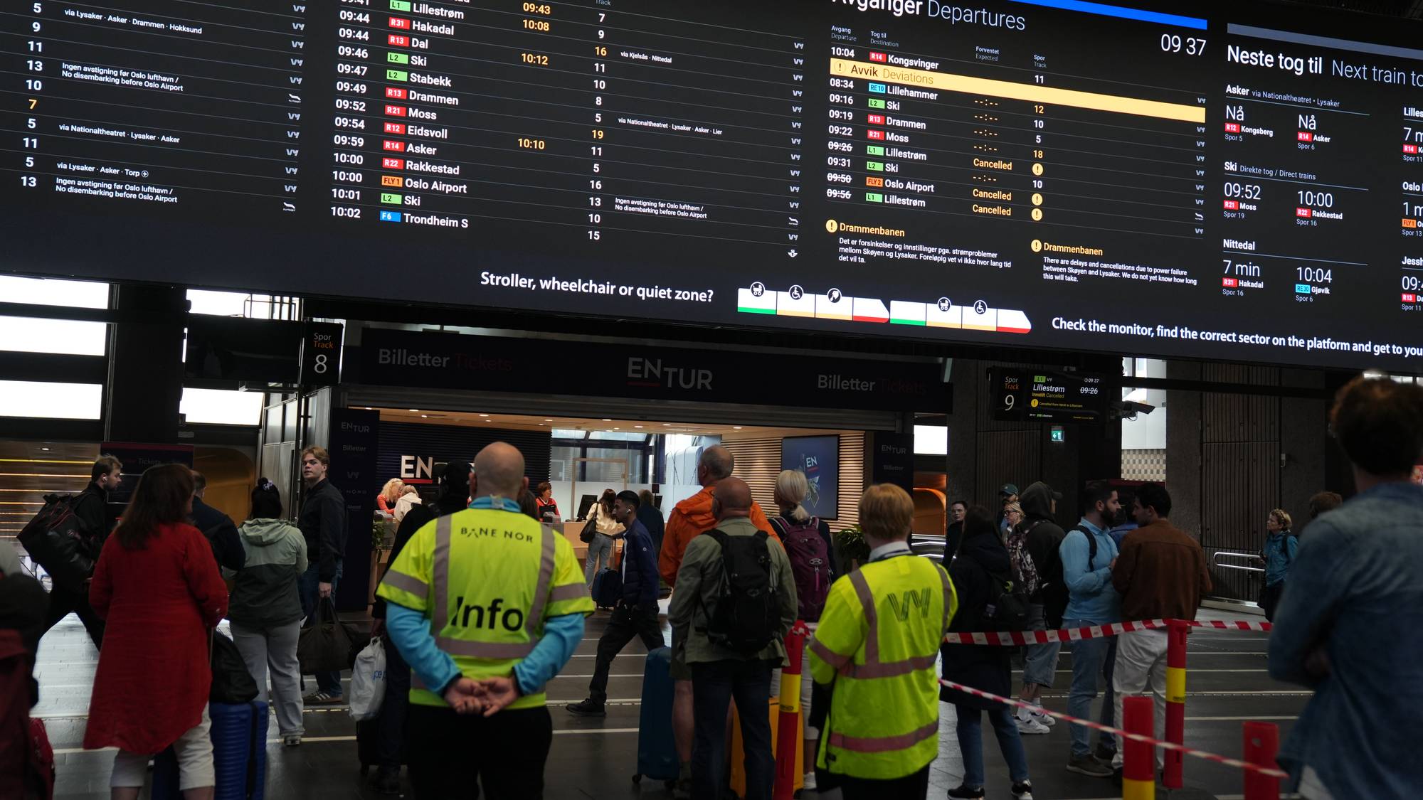 Reisende ser på store informasjonstavler med togavganger og meldinger om avvik på en togstasjon.