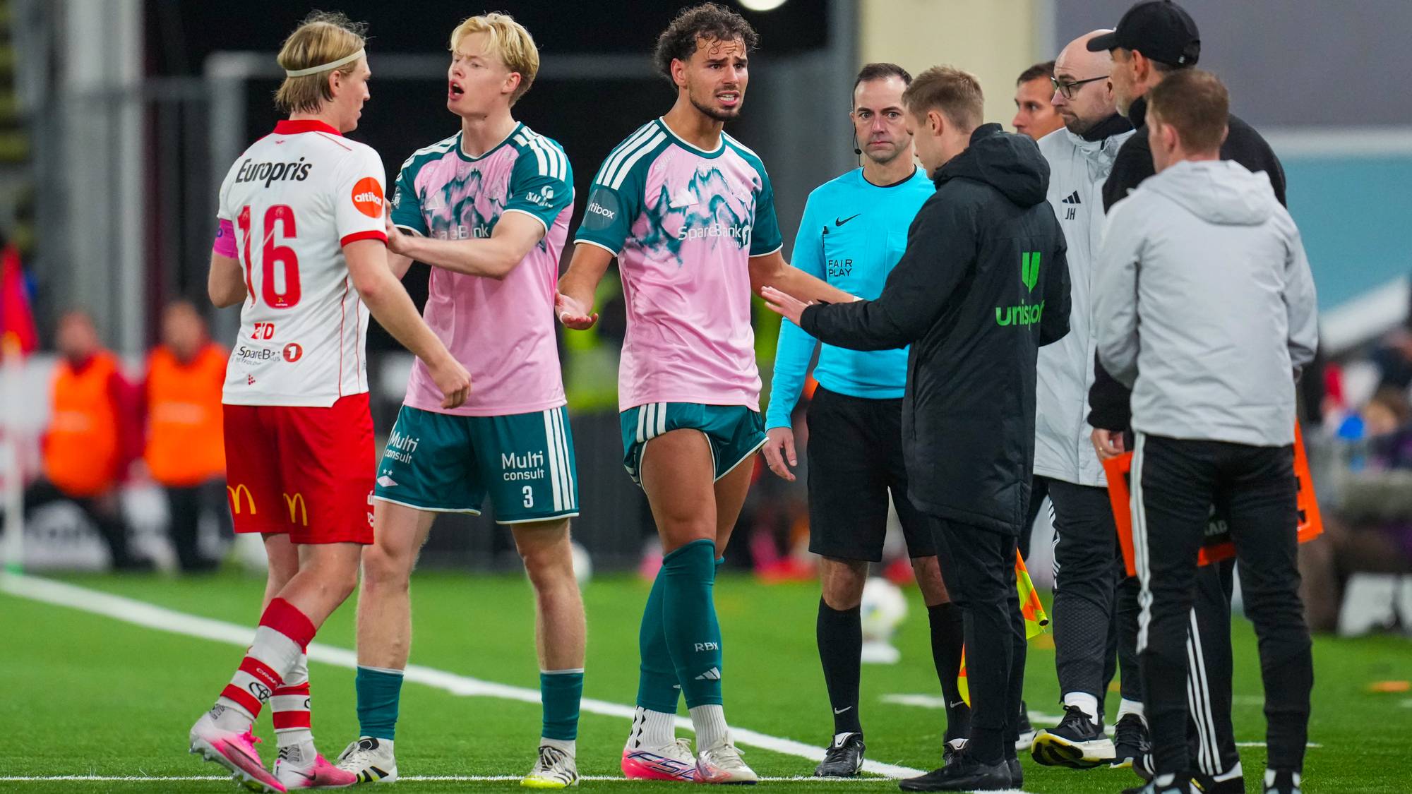 Fotballspillere i rosa drakter diskuterer med dommeren på banen. (Bildebeskrivelsen er laget av en KI-tjeneste)