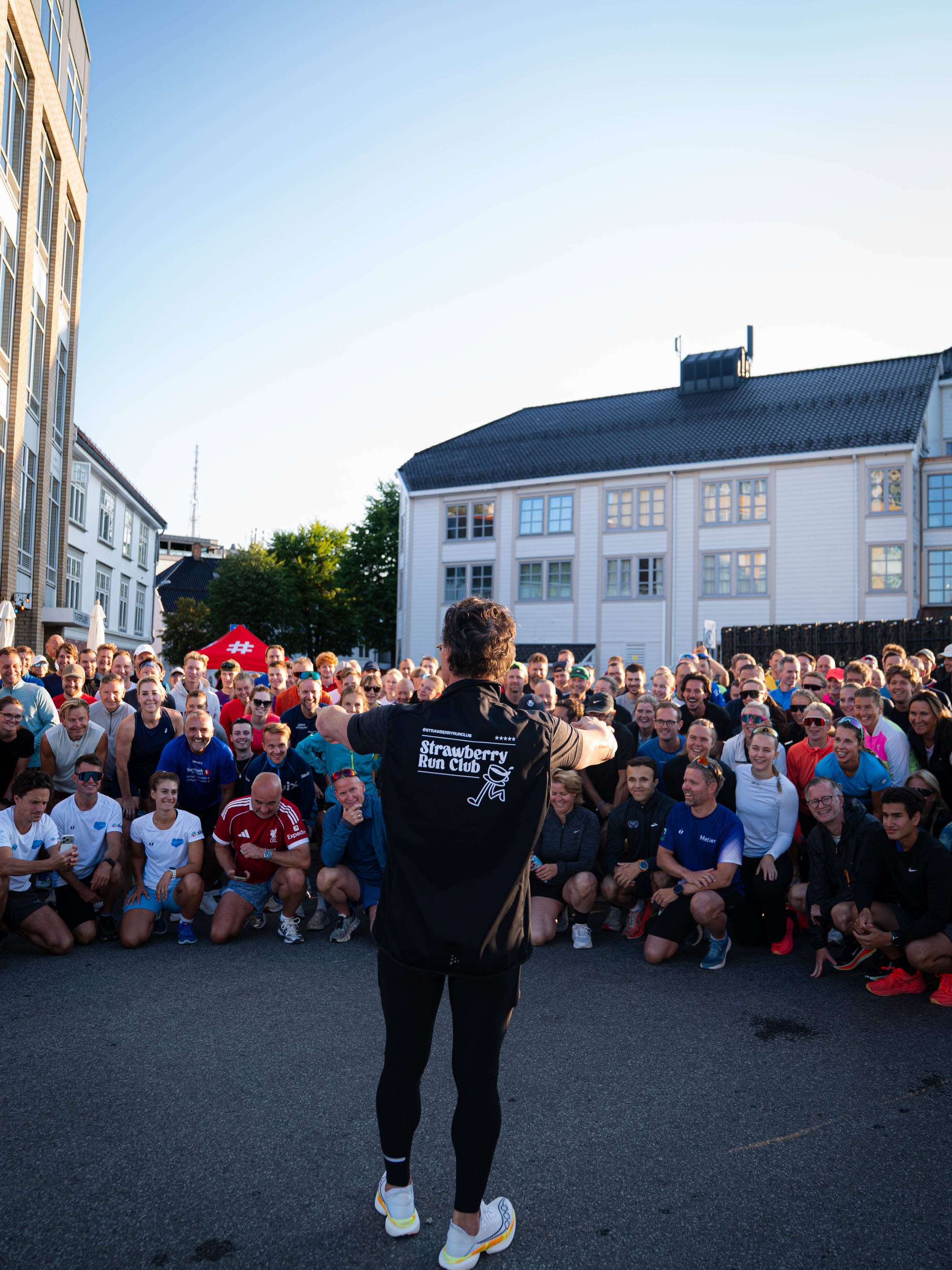 En gruppe løpere samlet rundt en instruktør foran en bygning.