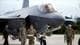 OGNEN TEOFILOVSKI / Reuters / NTB To personer i militærdress og en pilot går sammen foran et F-35-fly. Den ene av de to i militærklær holder et dokument. Omgivelsene viser en militær flyplass med klar himmel i bakgrunnen. Det er flere personer og fly i horisonten. (Bildebeskrivelsen er laget av en KI-tjeneste)