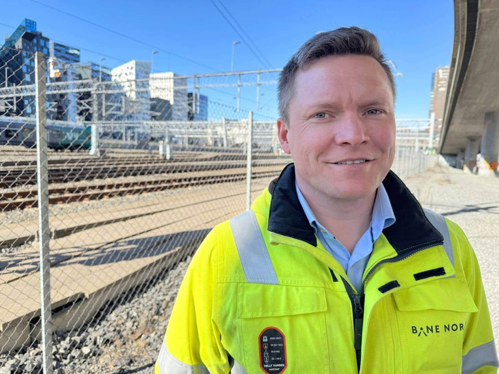 En mann med synlighetsjakke står ved et togspor