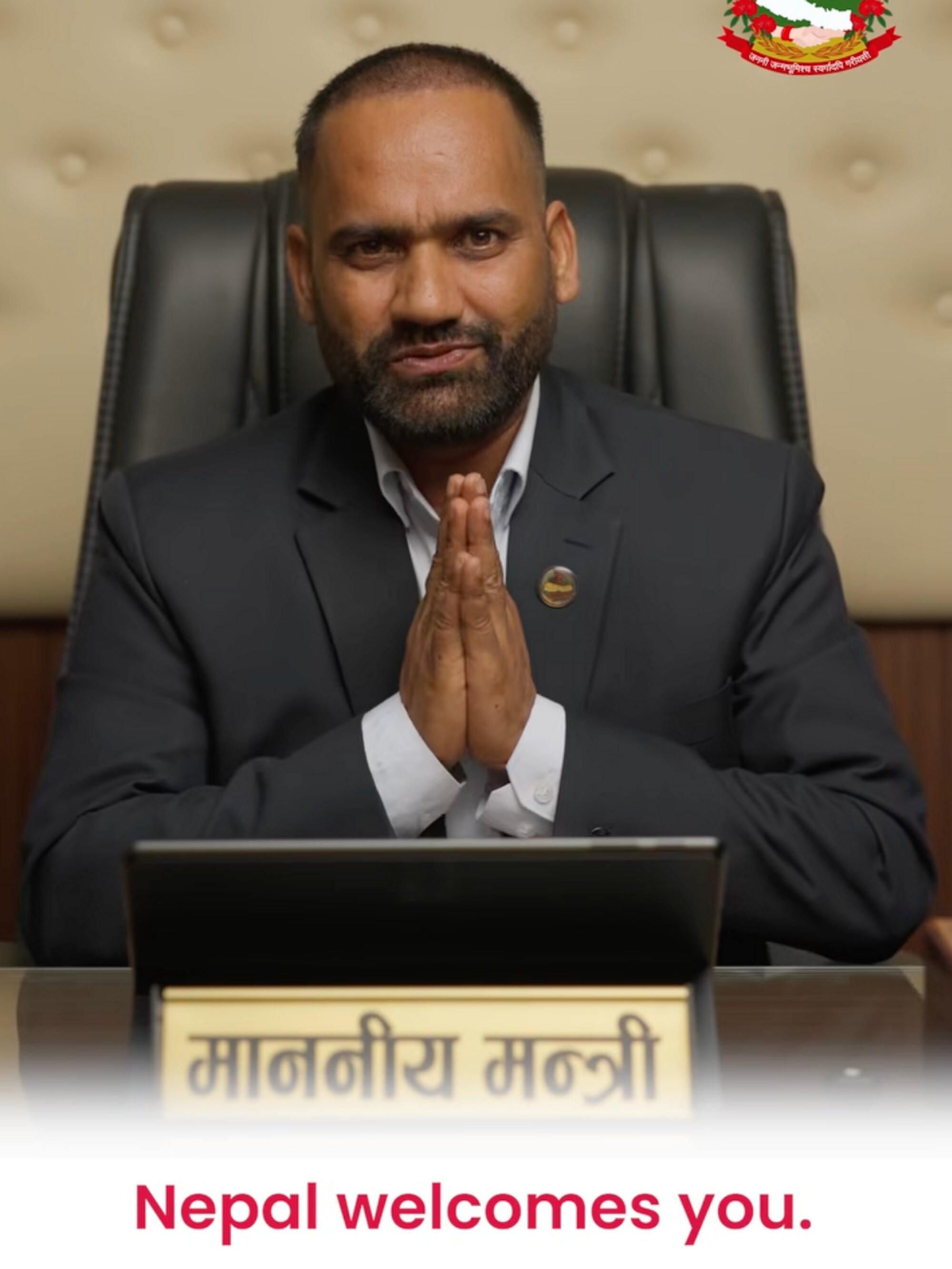 Illustrasjon av en mann i dress som hilser med samlede hender foran et skilt med nepalsk tekst. (Bildebeskrivelsen er laget av en KI-tjeneste)