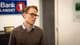 Frode Meskau / NRK En mann står i en bankfoaje, kledd i en brun genser og blå skjorte. I bakgrunnen er et skilt med logoen til SpareBank 1. Vegger og interiør gir et moderne og profesjonelt inntrykk. (Bildebeskrivelsen er laget av en KI-tjeneste)