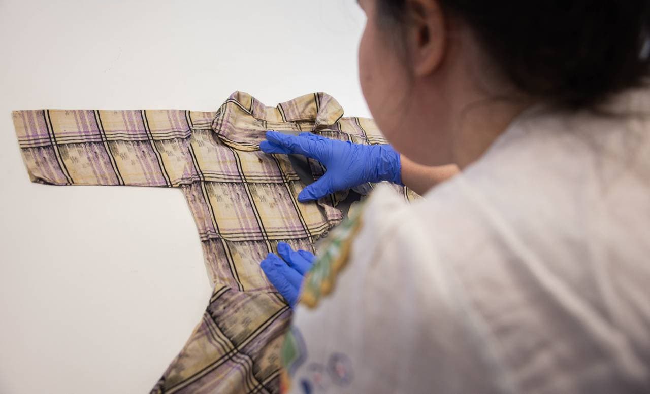 Tekstilkonservator Philippa Moxon ser på Ørnerovetkjolen. Bilde tatt over skulderen hennes.
