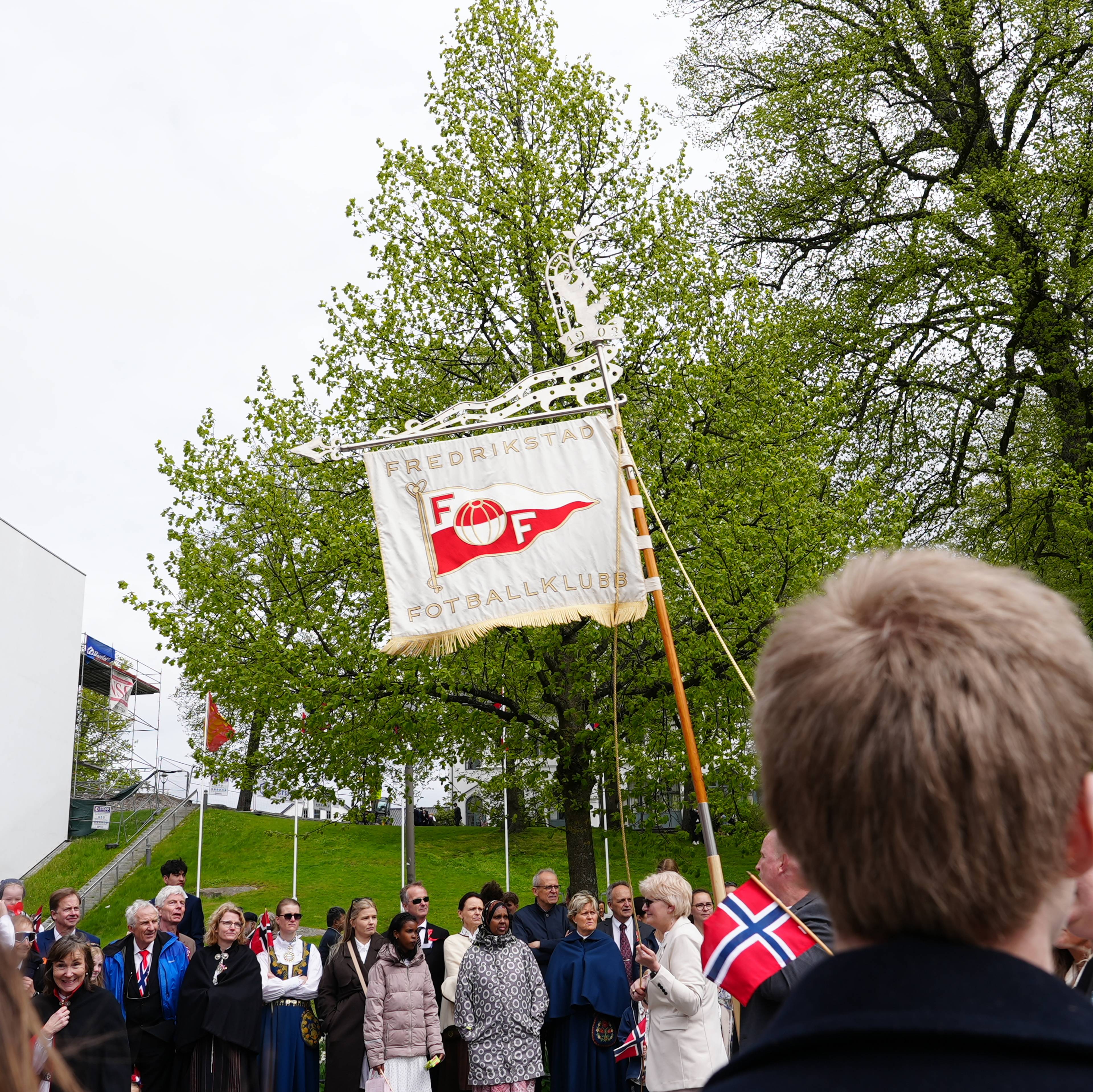 Flagg med FFK på i 17.mai-toget med masse folk rundt.