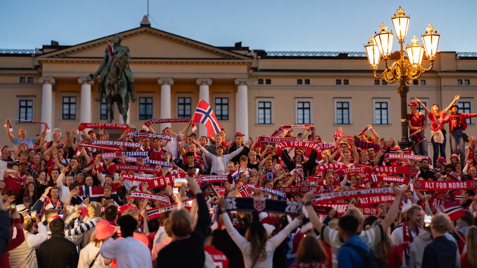 Supportere med norske flagg og skjerf feirer foran Slottet i Oslo. (Bildebeskrivelsen er laget av en KI-tjeneste)