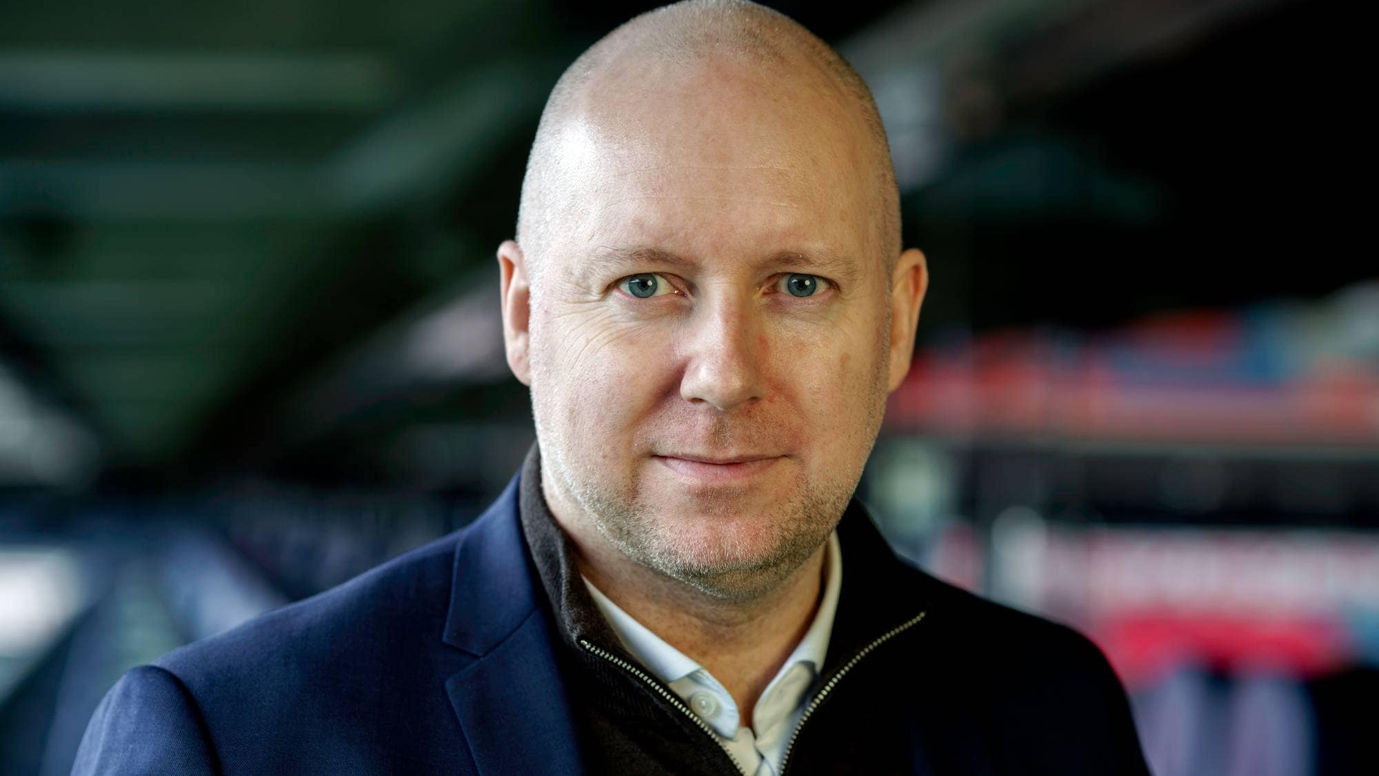 Portrett av en skallet mann i mørk dressjakke med skjorte og genser under. (Bildebeskrivelsen er laget av en KI-tjeneste)