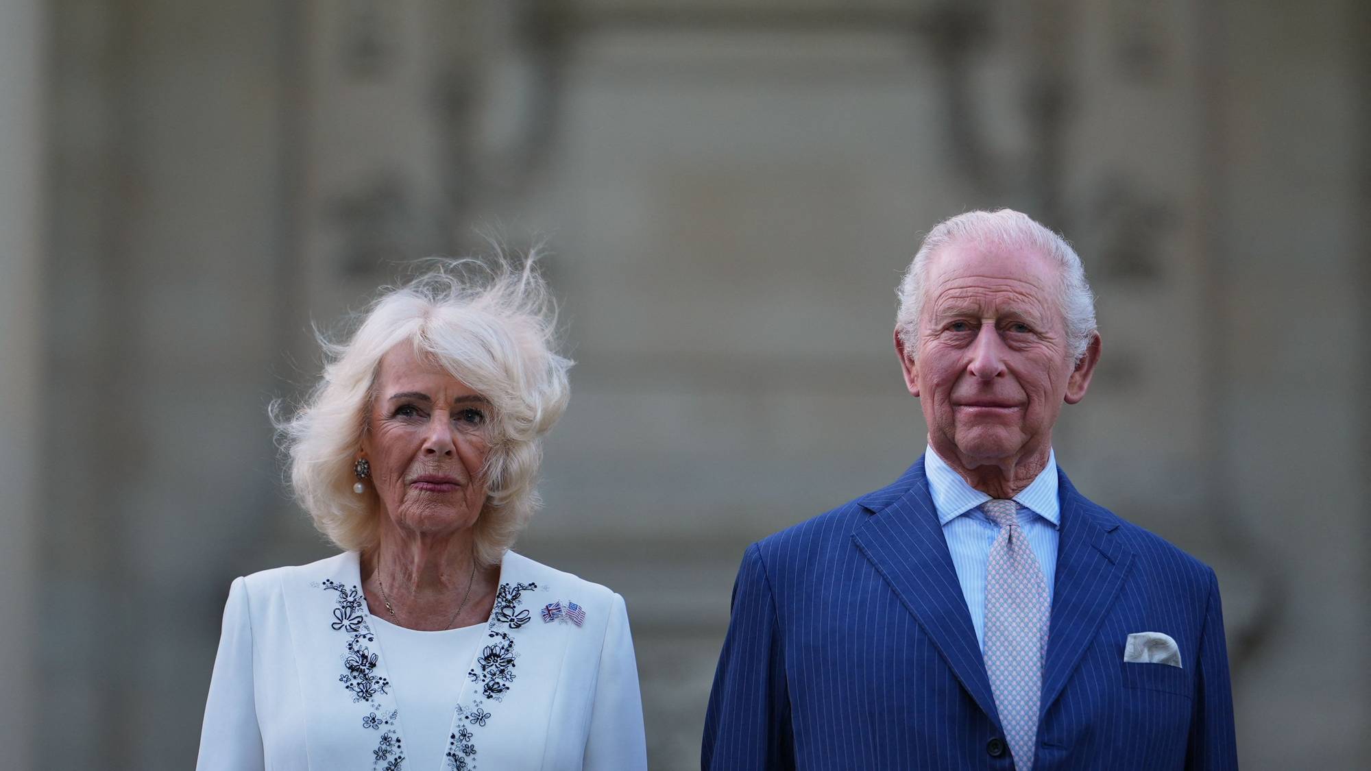 Kong Charles og dronning Camilla poserer foran en bygning. Kongen har blå dress, hvit skjorte og lyseblå slips. Dronningen har hvit drakt med broderte detaljer. (Bildebeskrivelsen er laget av en KI-tjeneste)