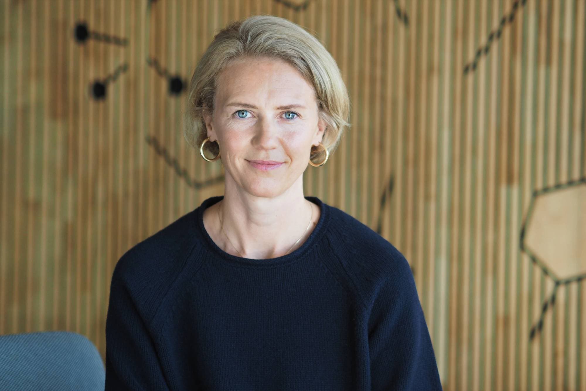 Overlege Ingrid Aas smiler forsiktig til kamera. Hun har kort, lyst hår, blå øyne og lys hud. Hun har på seg en svart genser.