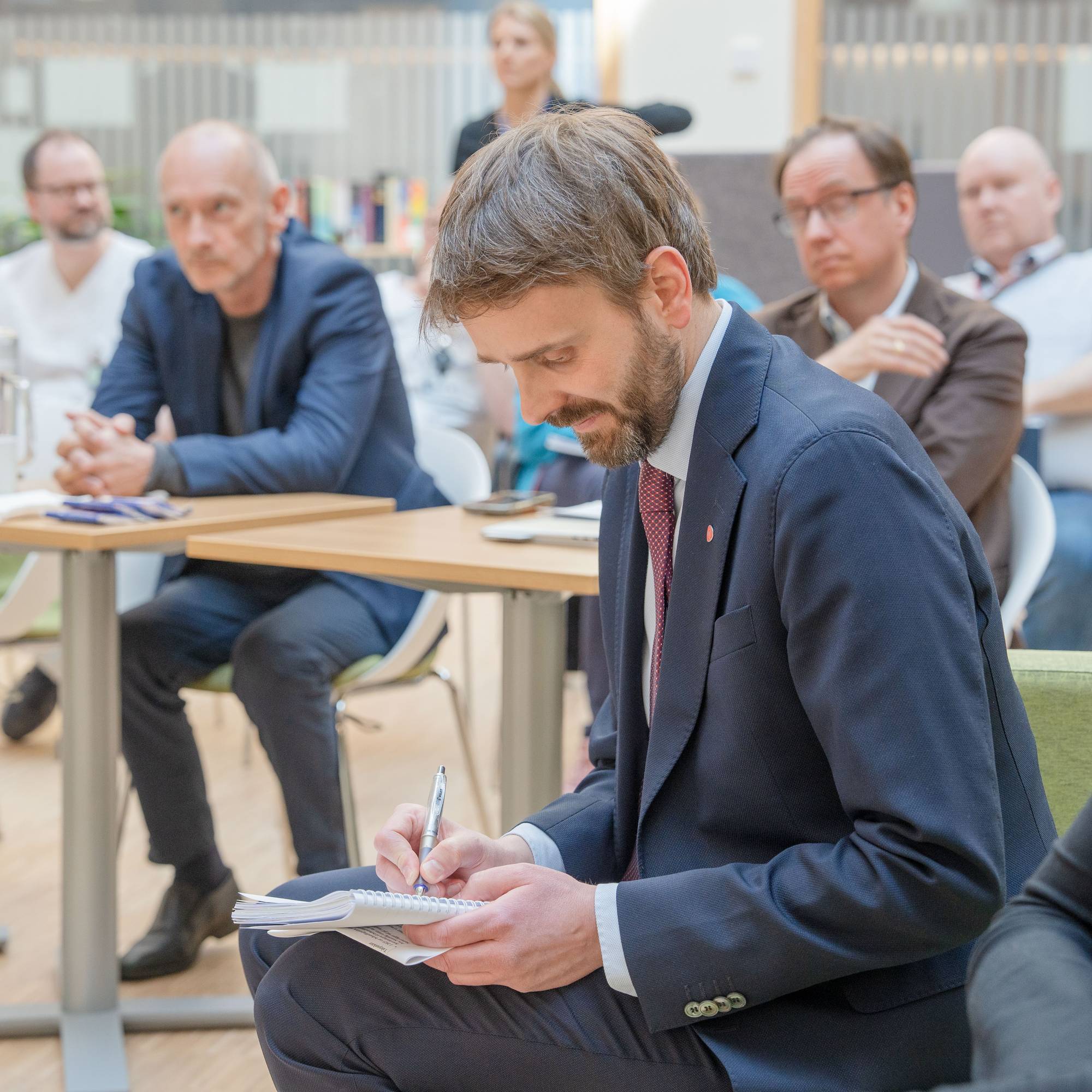 Helseminister Jan Christian Vestre noterer med ansatte i bakgrunnen.