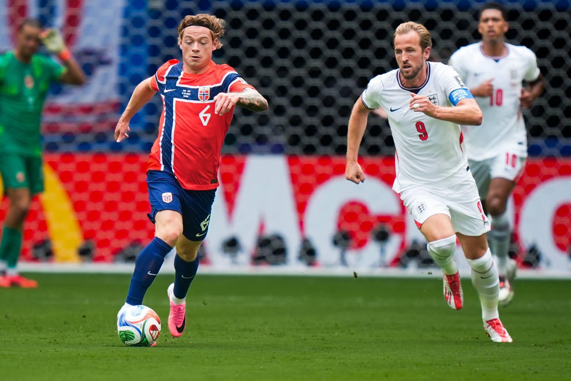 Norsk spiller med ballen forfølges av engelske Harry Kane i en fotballkamp. (Bildebeskrivelsen er laget av en KI-tjeneste)