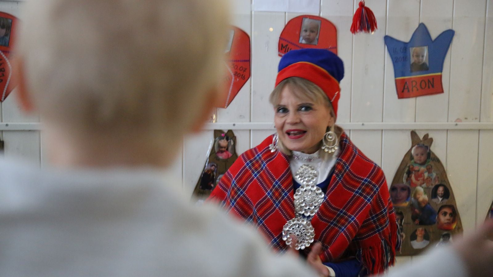 Kvinne i samedrakt i samisk barnehage i Oslo forteller historier til barna. Man ser ryggen av et barn i bildet.