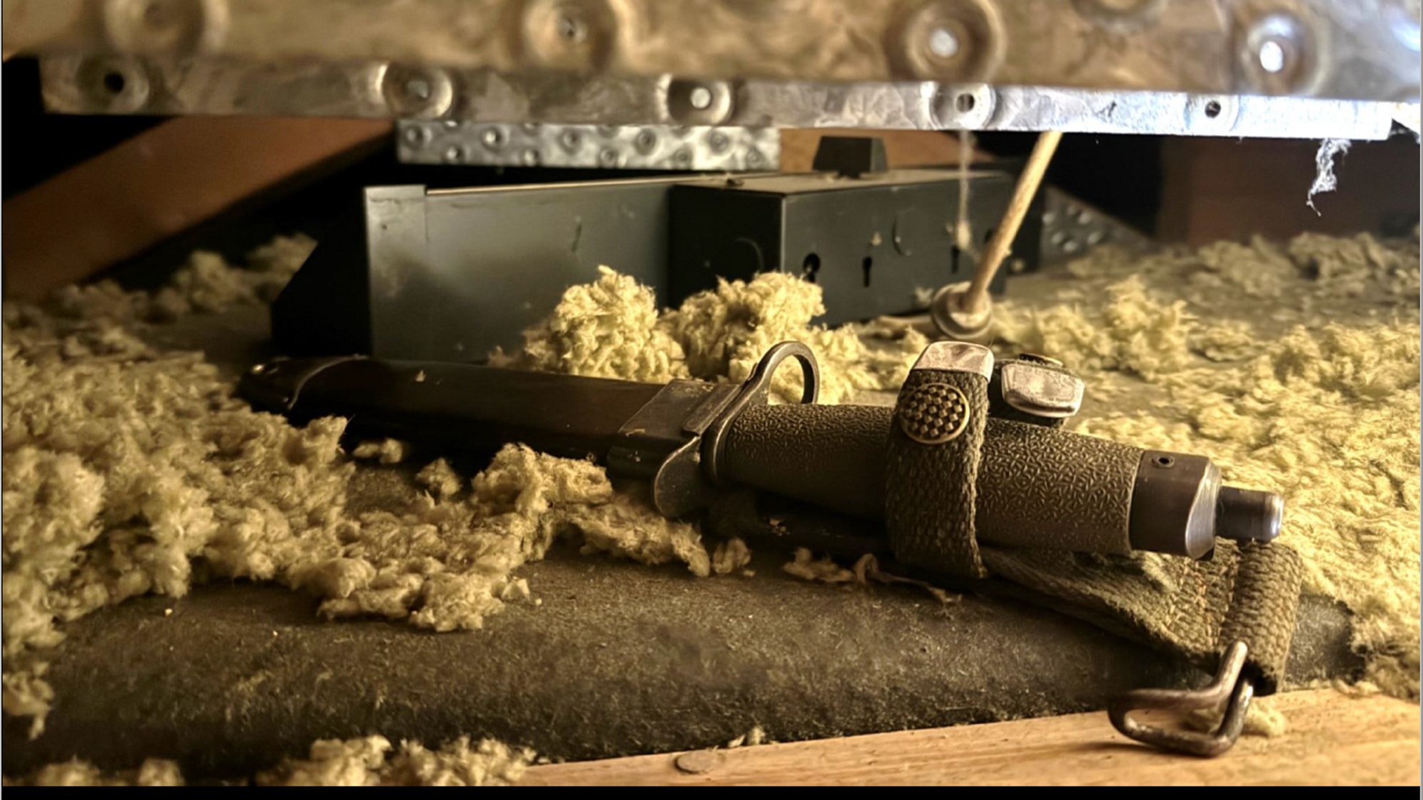 En bajonett ligger på loftet sammen med isoleringsmateriale. 