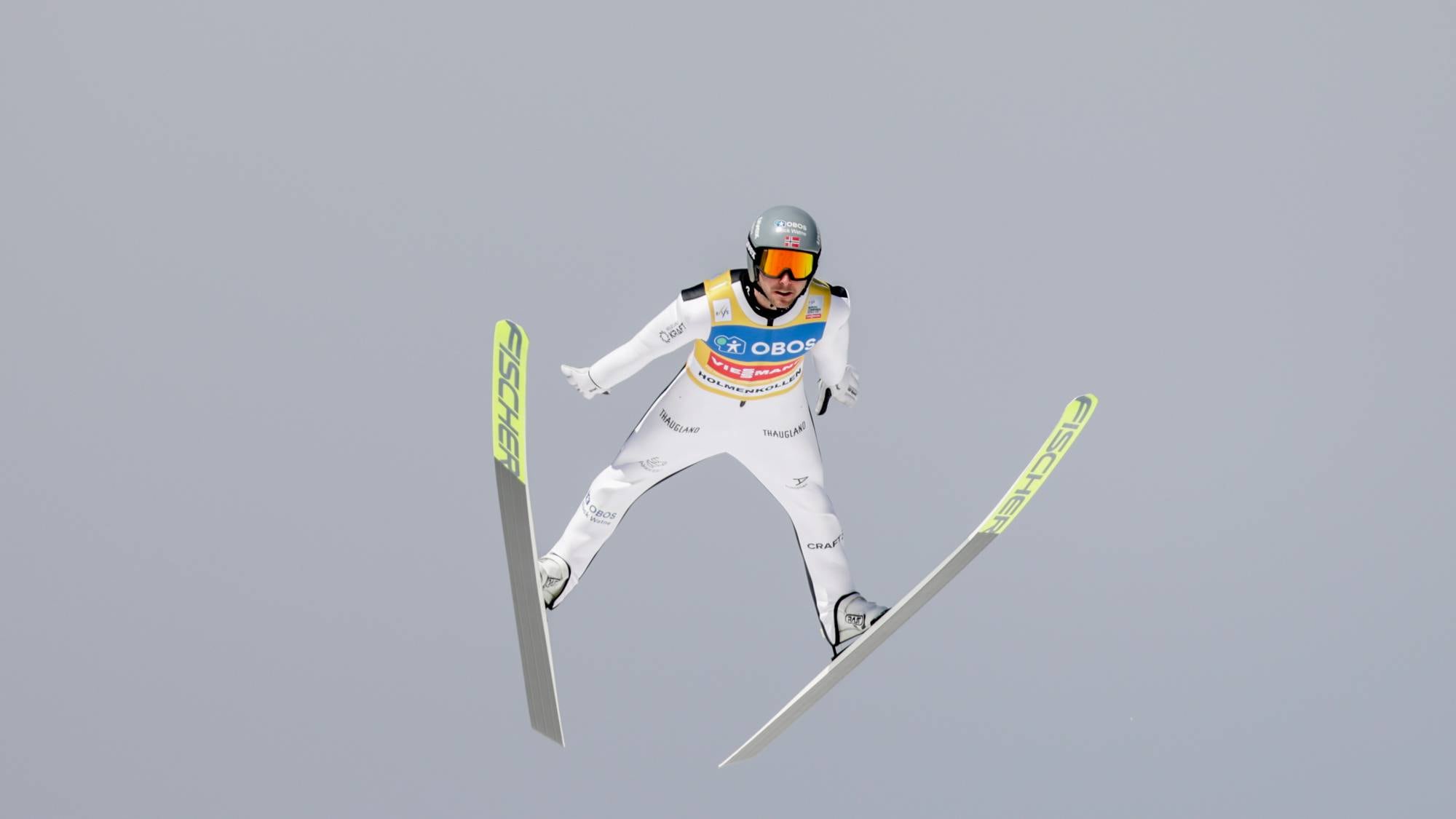 Skihopper i svevet med skiene i V-posisjon mot en grå himmel. (Bildebeskrivelsen er laget av en KI-tjeneste)