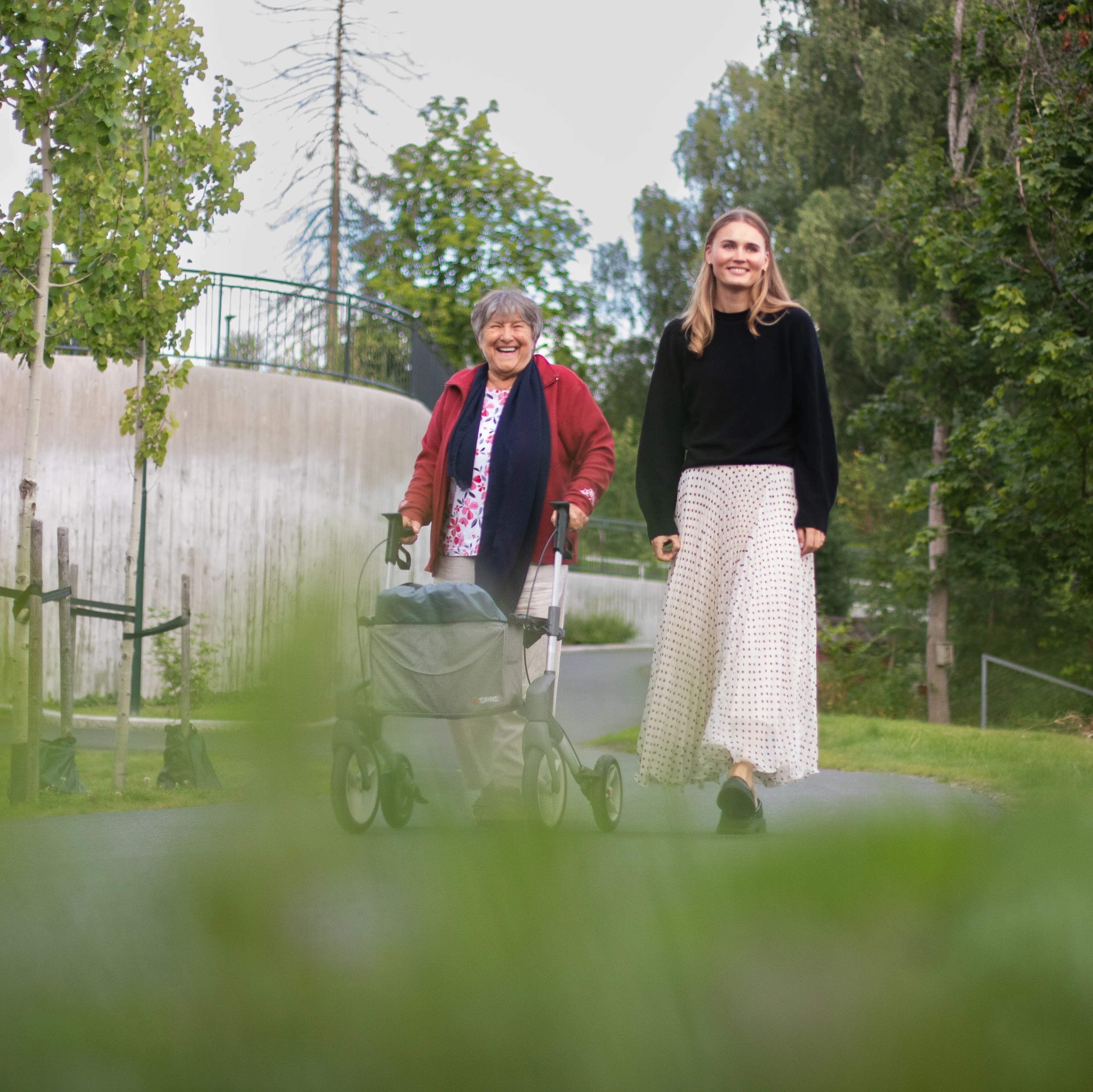 en eldre kvinne med rullator går  ute sammen med en ung kvinne