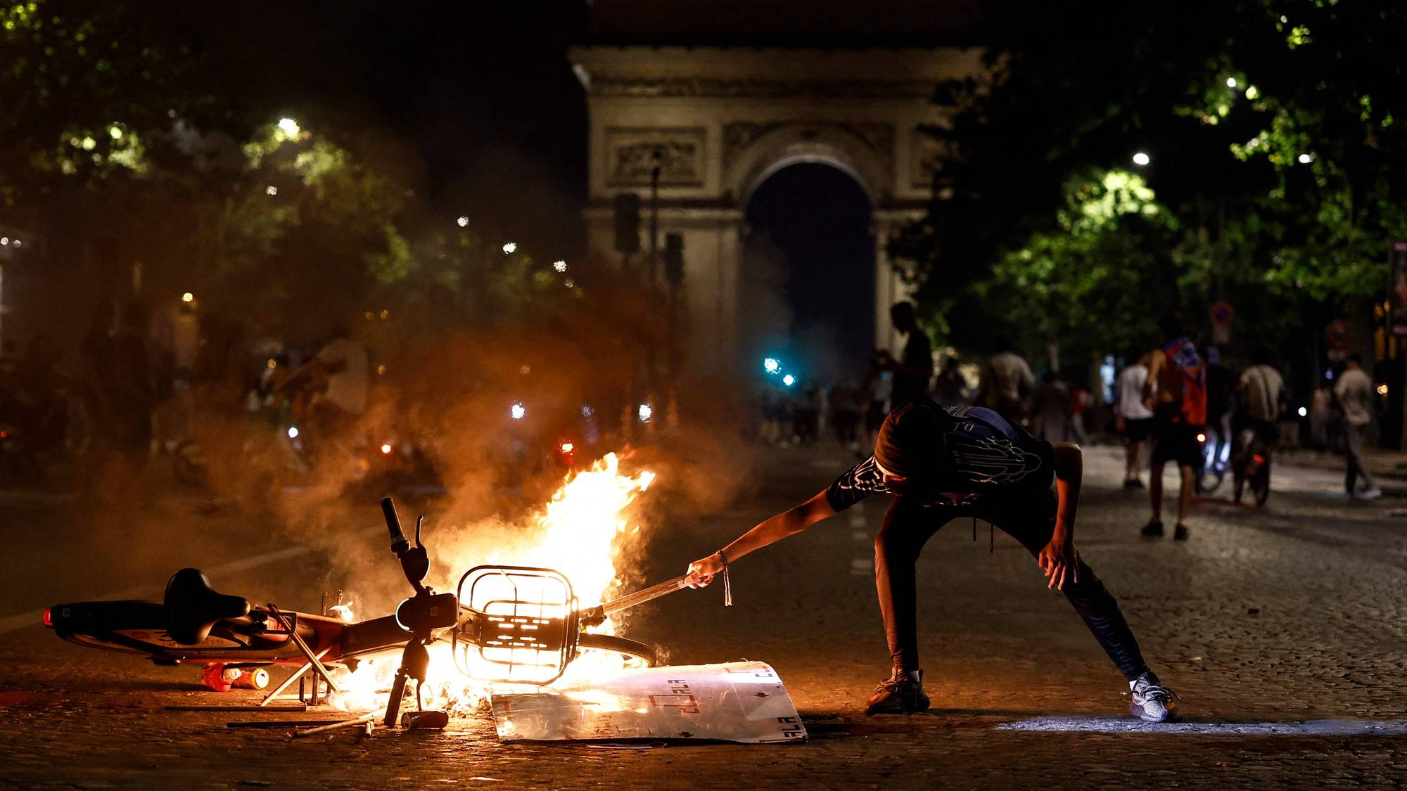 En mann tenner en fakkel ved en brennende sykkel foran triumfbuen i Paris