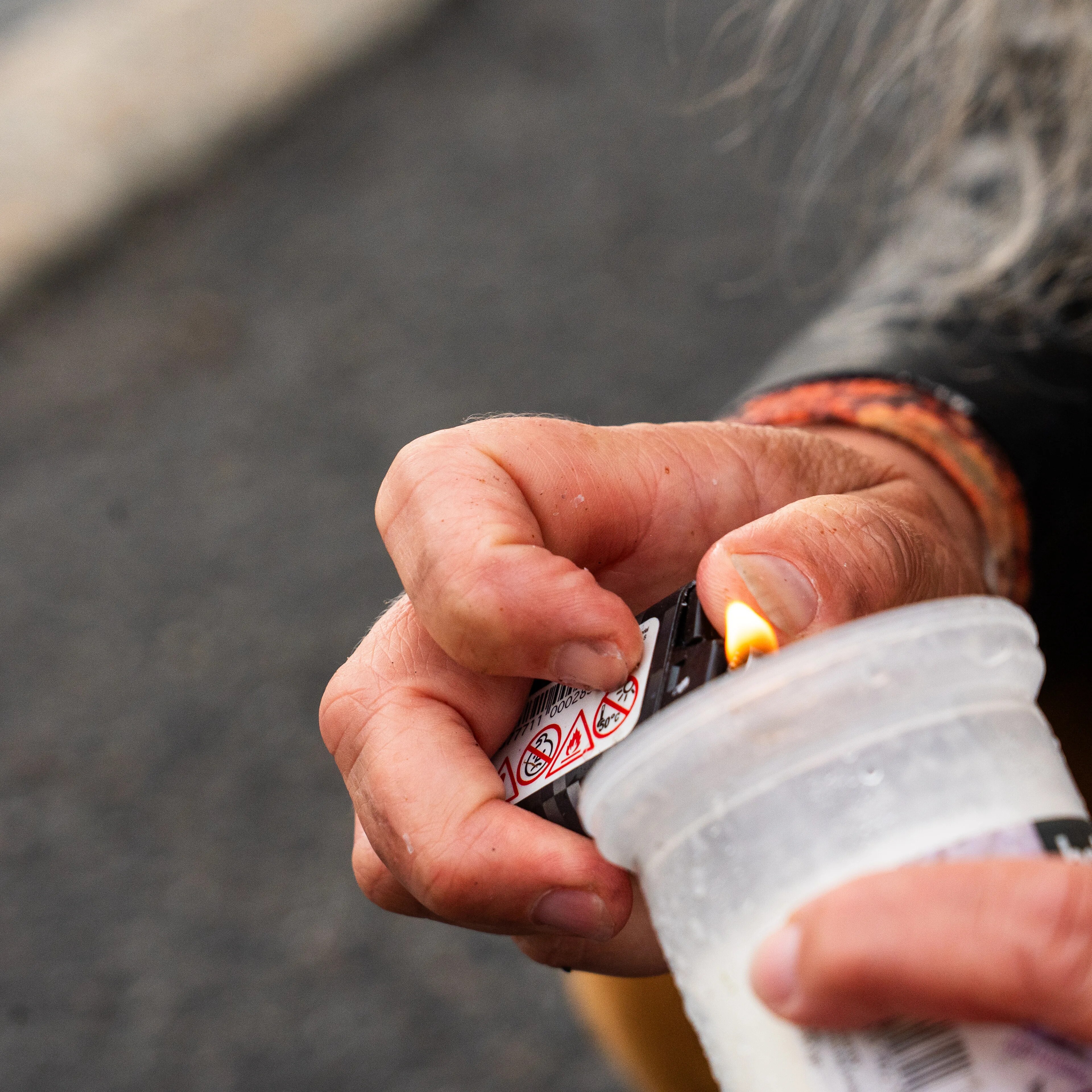 En person tenner et stearinlys i en plastbeholder med en lighter. (Bildebeskrivelsen er laget av en KI-tjeneste)