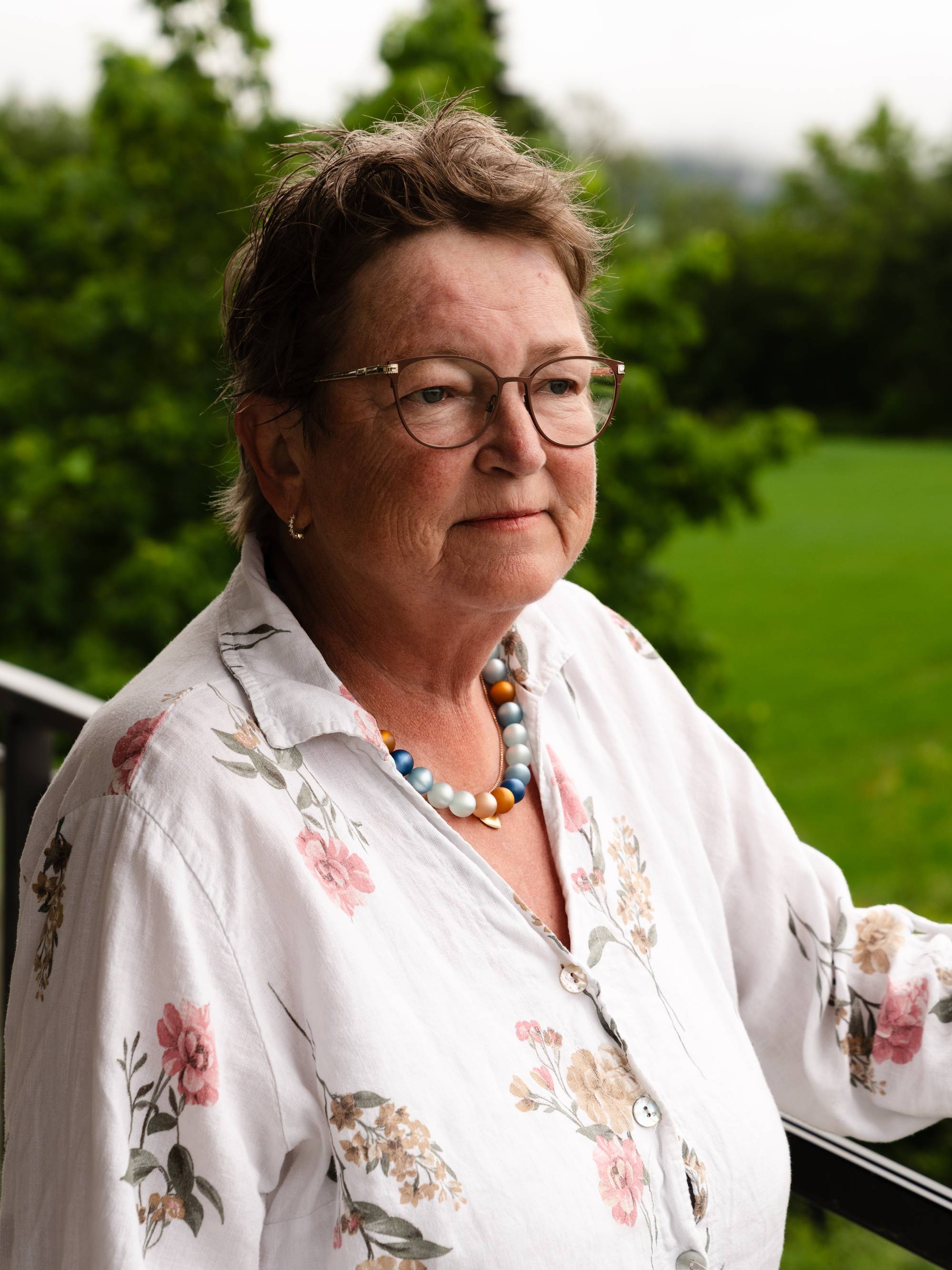 bilde av person på en veranda med grønne trær i bakgrunnen. 