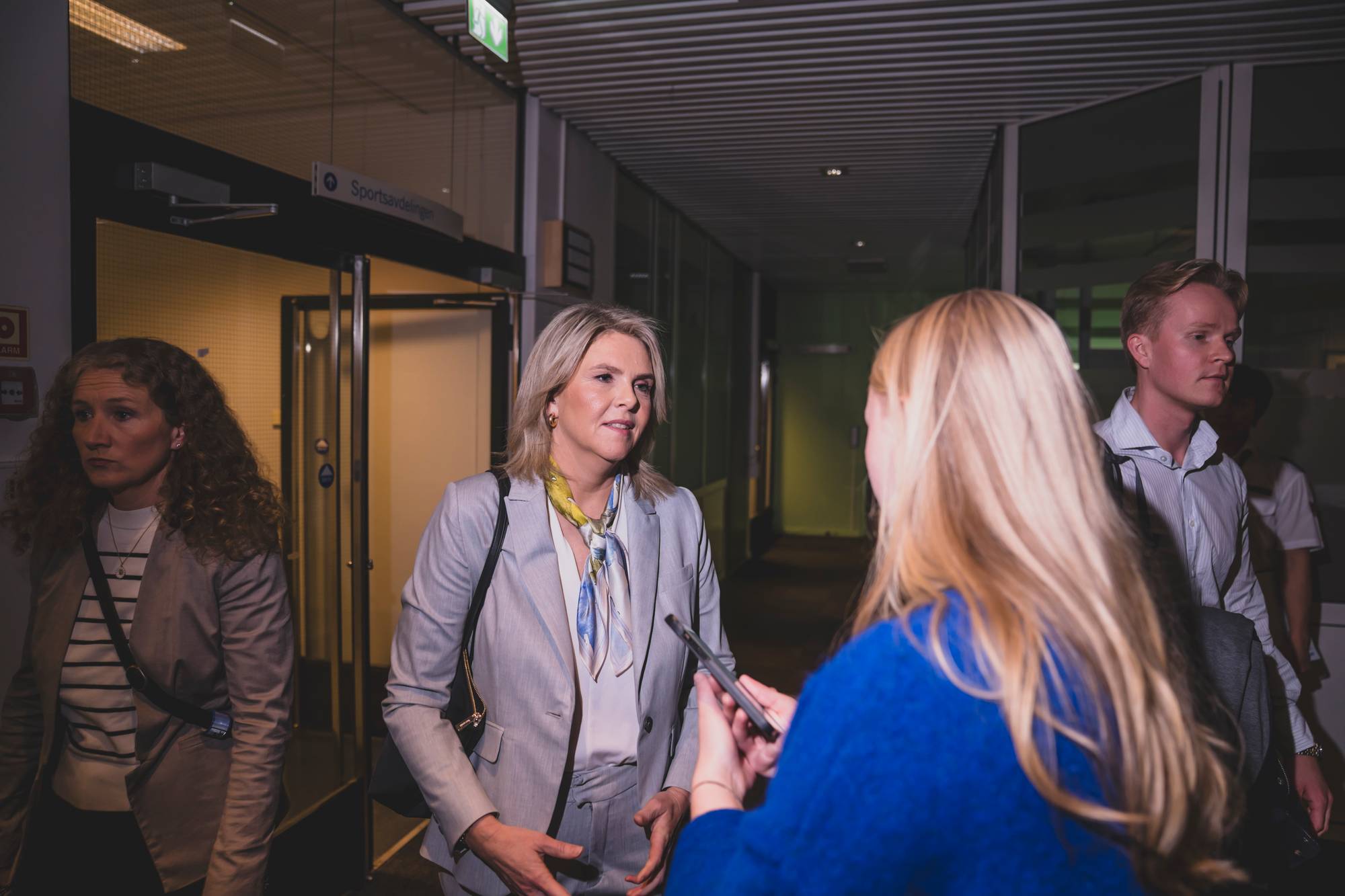 Sylvi Listhaug blir intervjuet av en journalist i en kontorkorridor. (Bildebeskrivelsen er laget av en KI-tjeneste)
