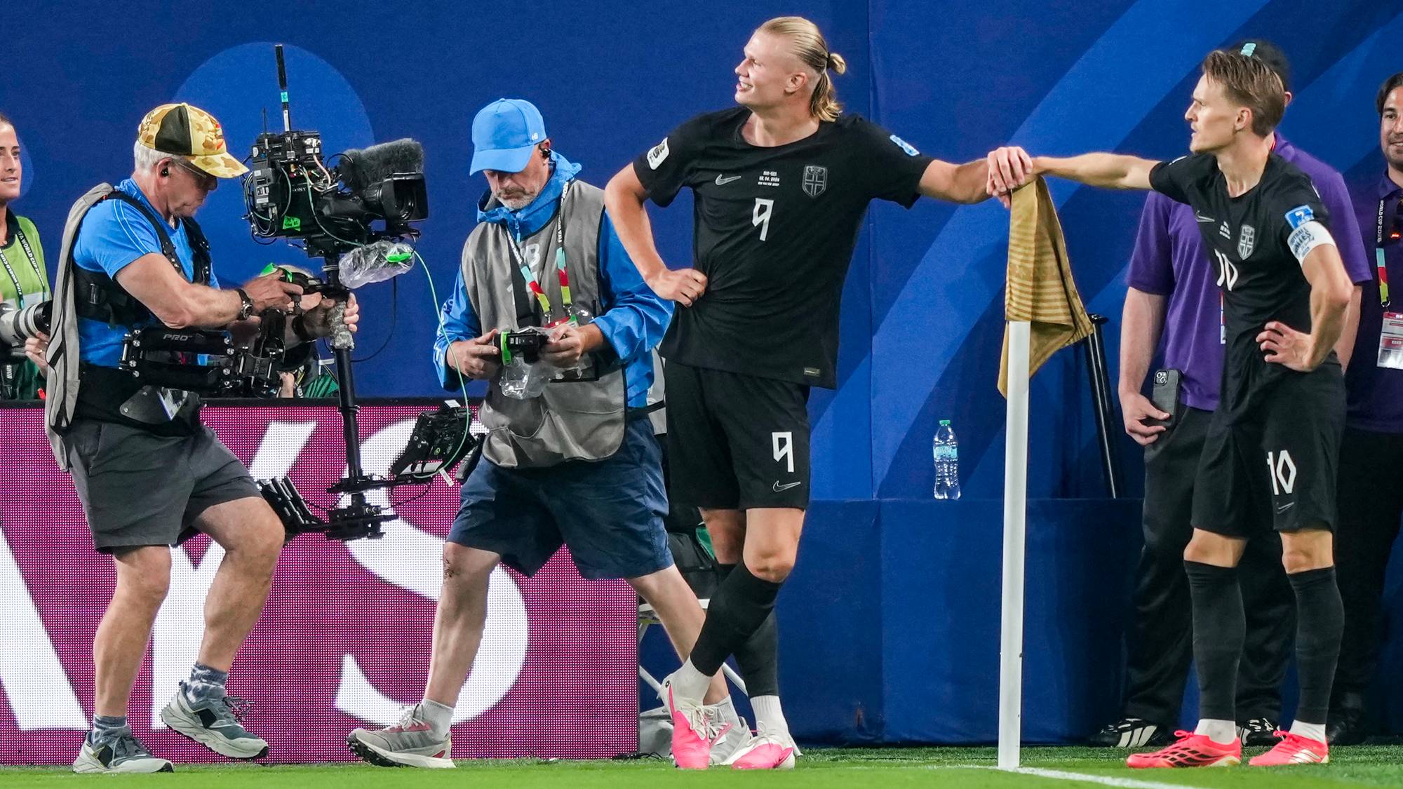 Erling Braut Haaland og Martin Ødegaard i samtale ved et hjørneflagg mens fotografer filmer. (Bildebeskrivelsen er laget av en KI-tjeneste)