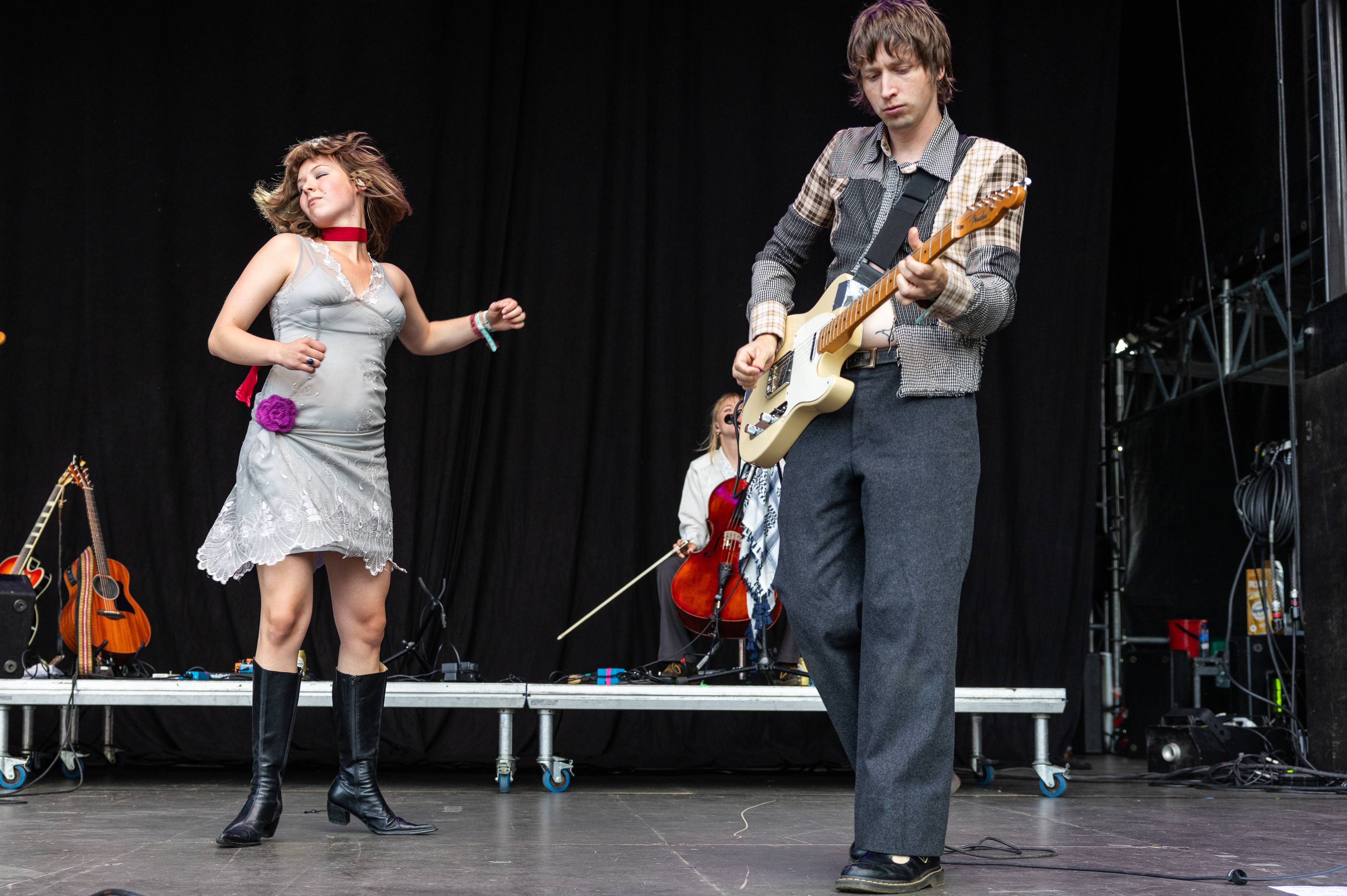 En kvinne danser ved siden av en gitarist på en konsertscene med svart bakgrunn.