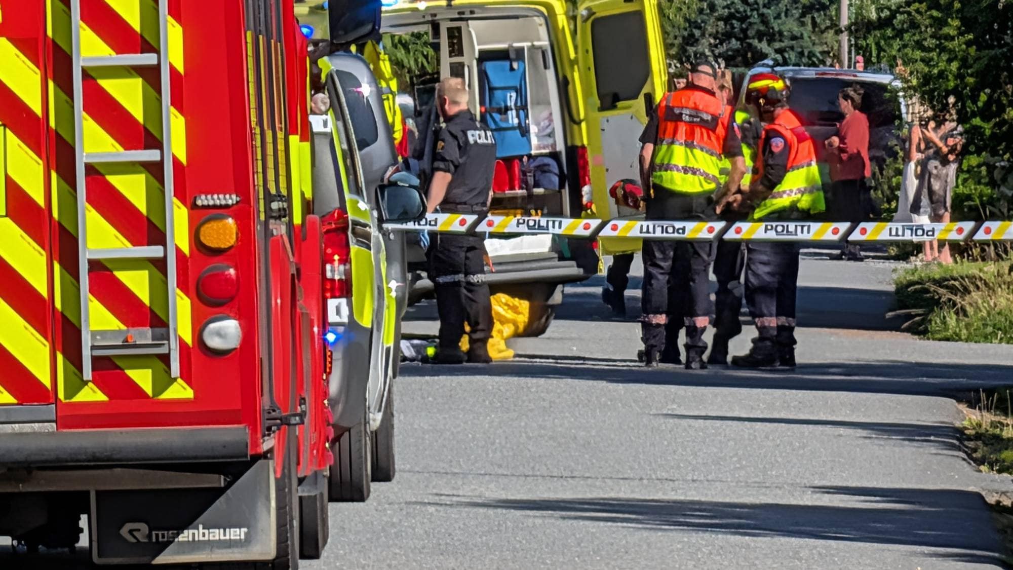 Politi og ambulansepersonell på et ulykkessted. Politibånd er spent opp foran utrykningskjøretøy. (Bildebeskrivelsen er laget av en KI-tjeneste)